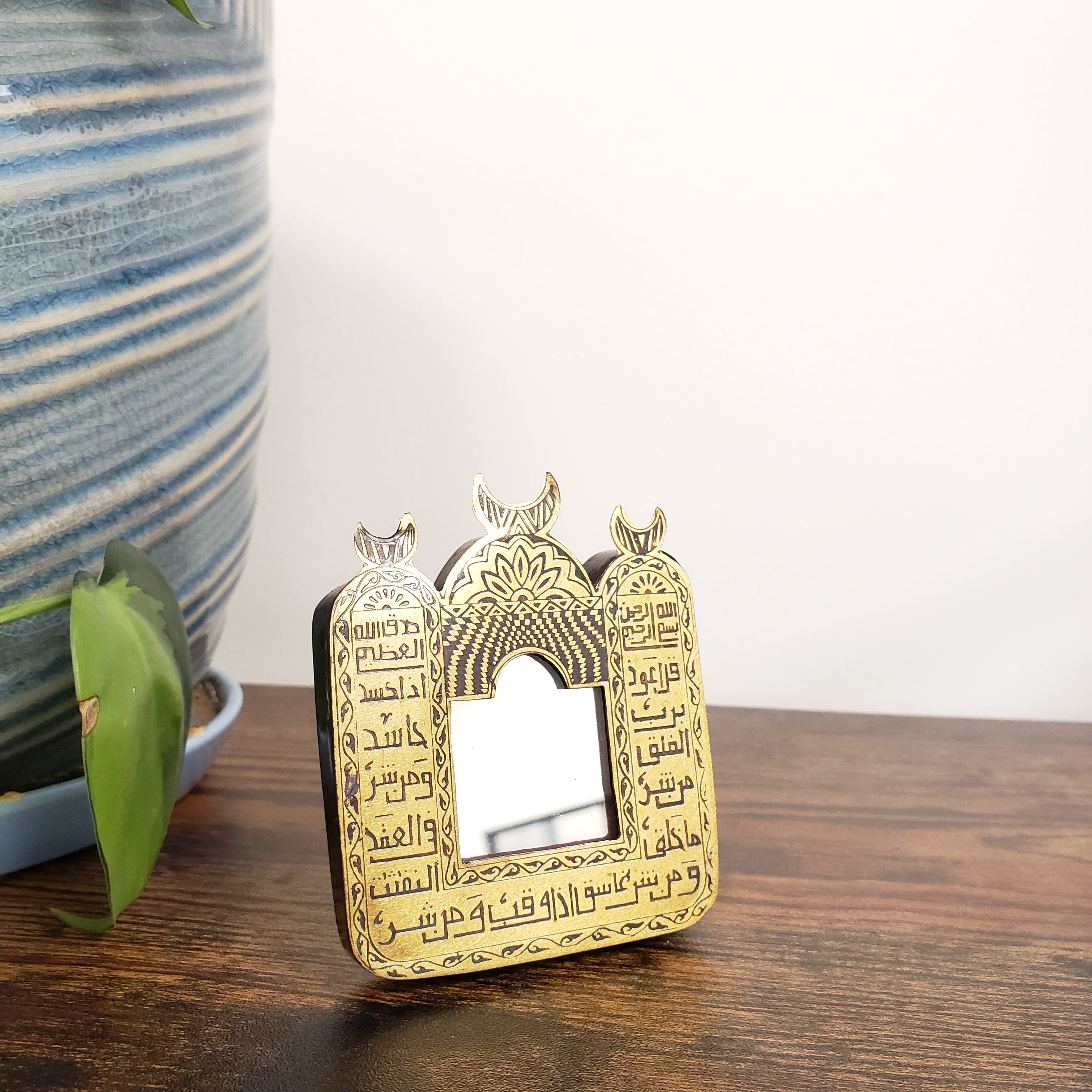 Decorative mirror with Arabic text on a wooden surface.