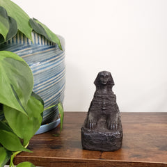 Decorative Egyptian sphinx on a wooden panel with plants in the foreground.