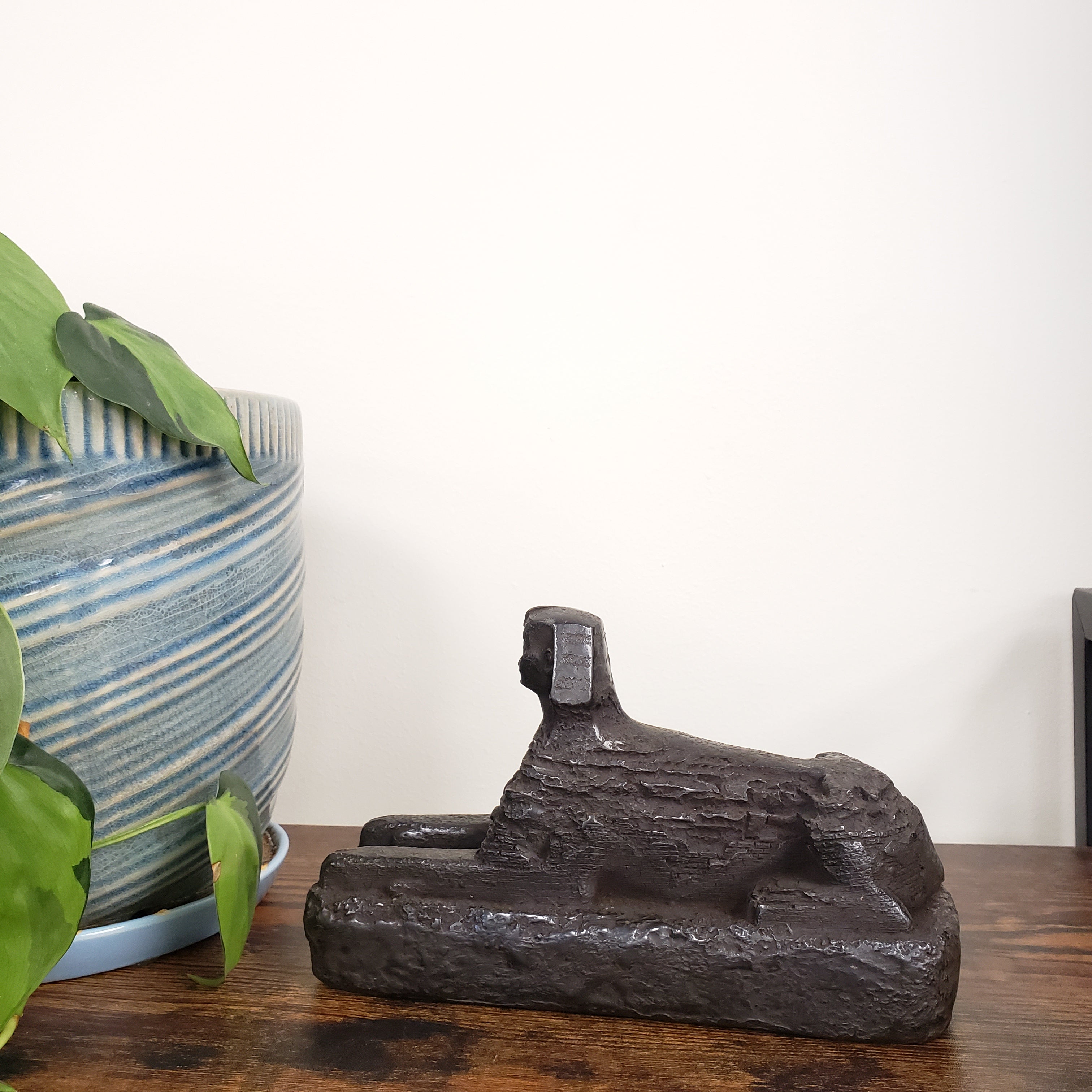 Decorative Egyptian sphinx on a wooden panel with a plant in the foreground