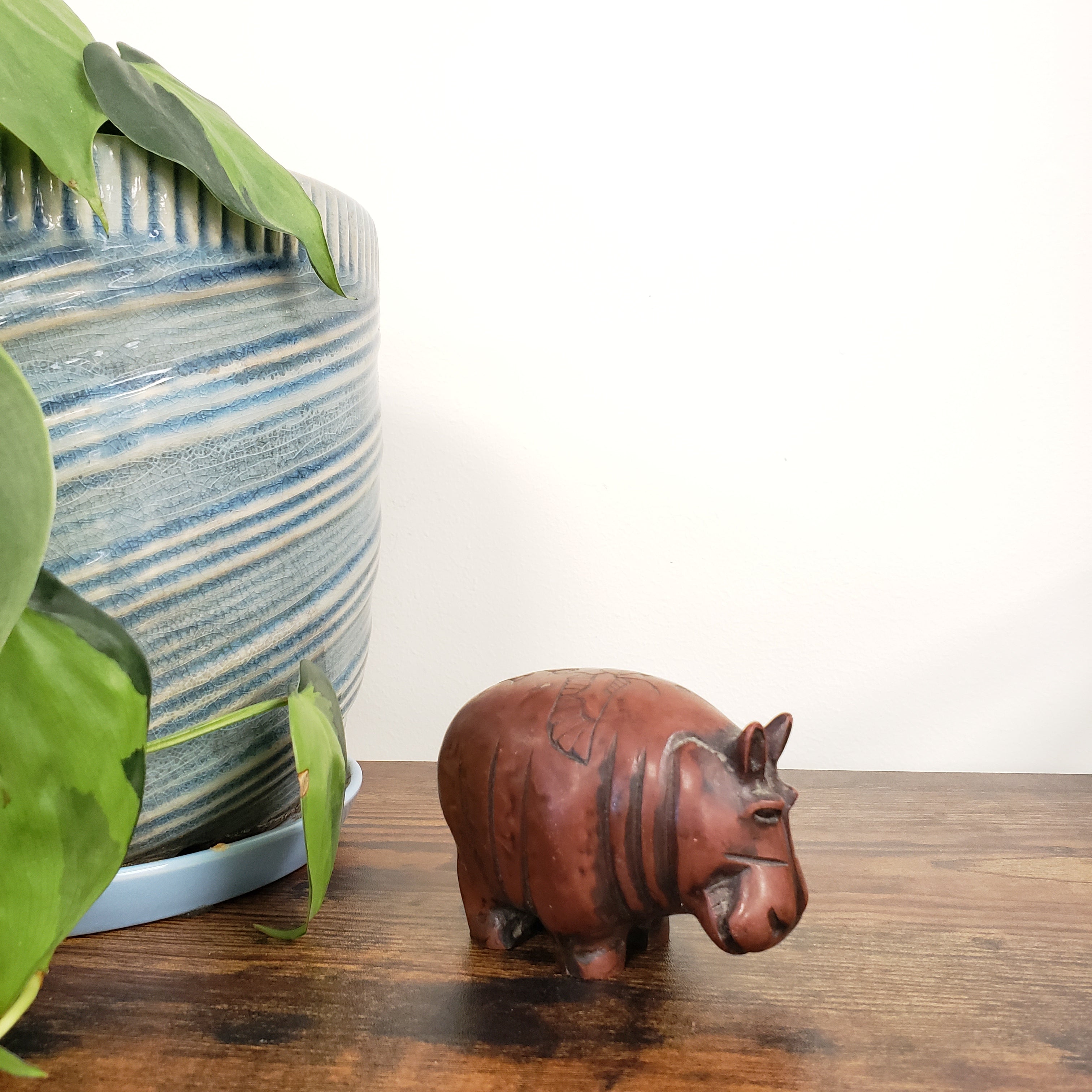 Decorative brown hippo figure on a wooden surface with green leaves in the foreground