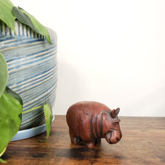 Decorative brown hippo figure on a wooden surface with green leaves in the foreground