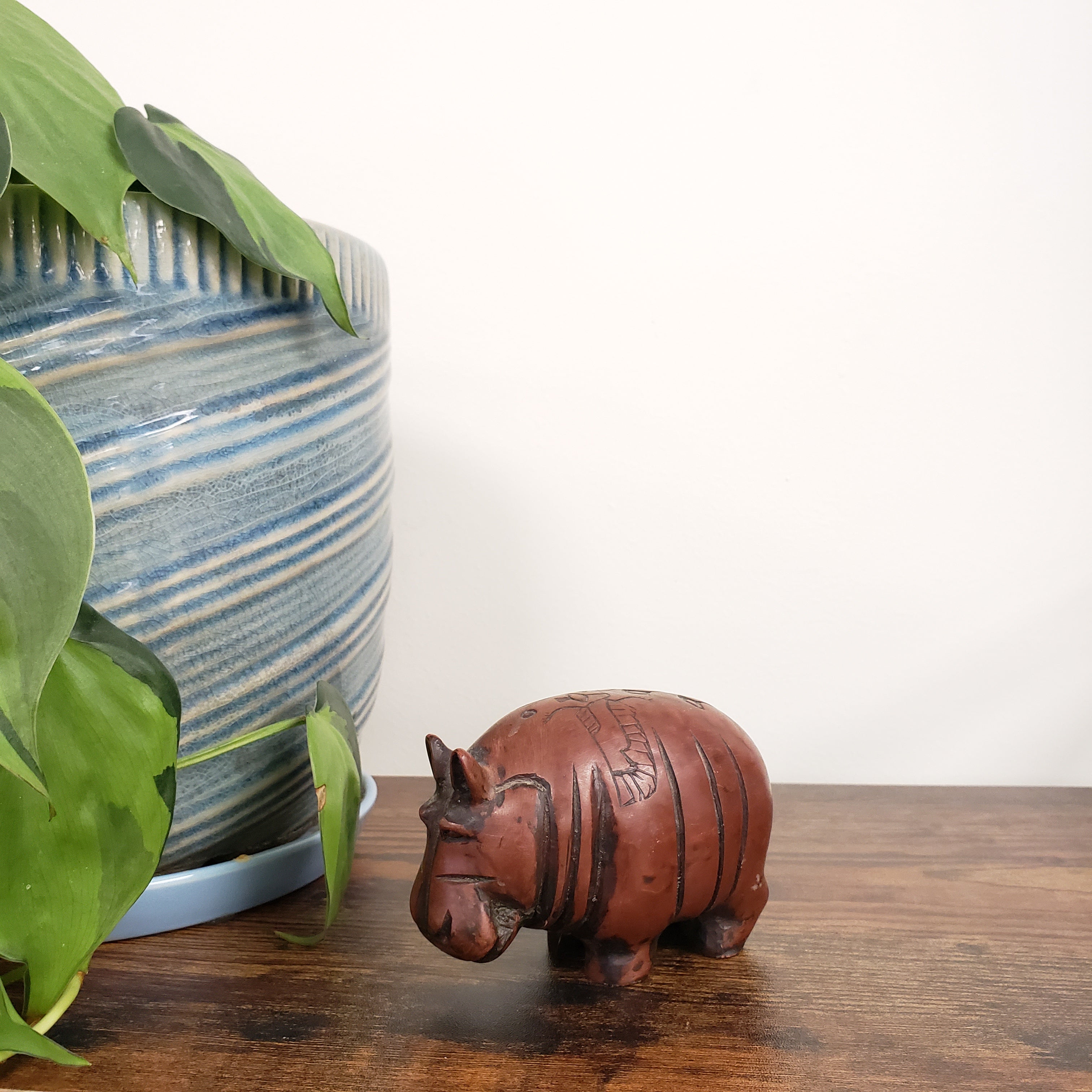 Decorative hippo statue on a wooden surface with plants in the foreground.