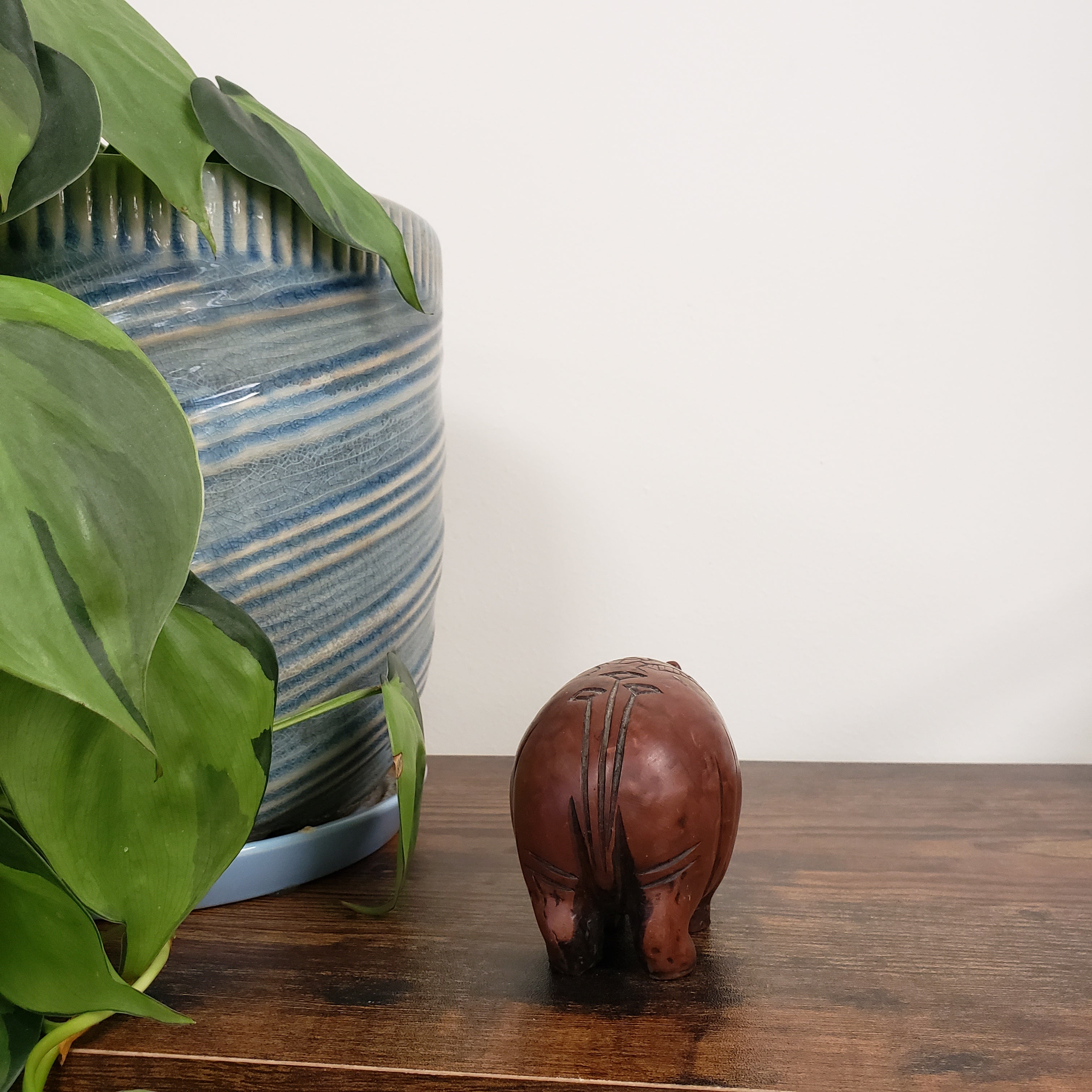 Decorative hippo statue on a shelf with plants and a striped pillow in the background
