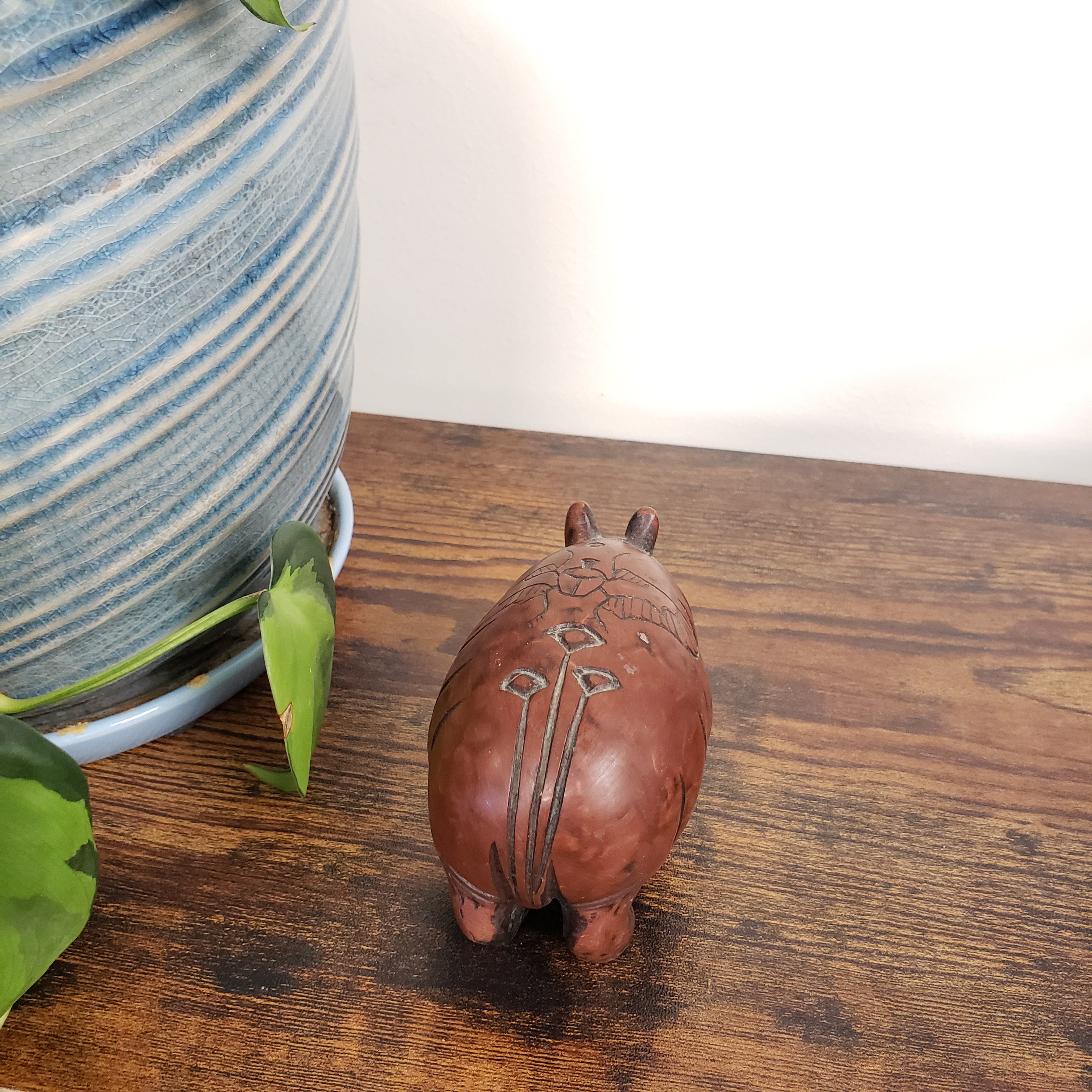 hippo statue with floral design on a wooden surface next to a striped ceramic pot.