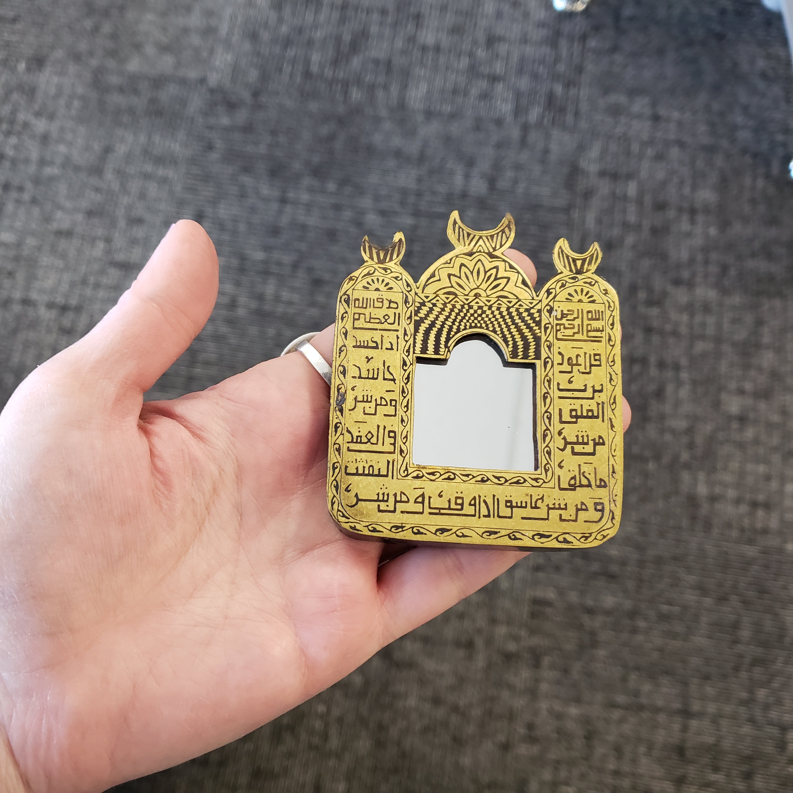Gold decorative item with Arabic text held in a hand against a textured gray background