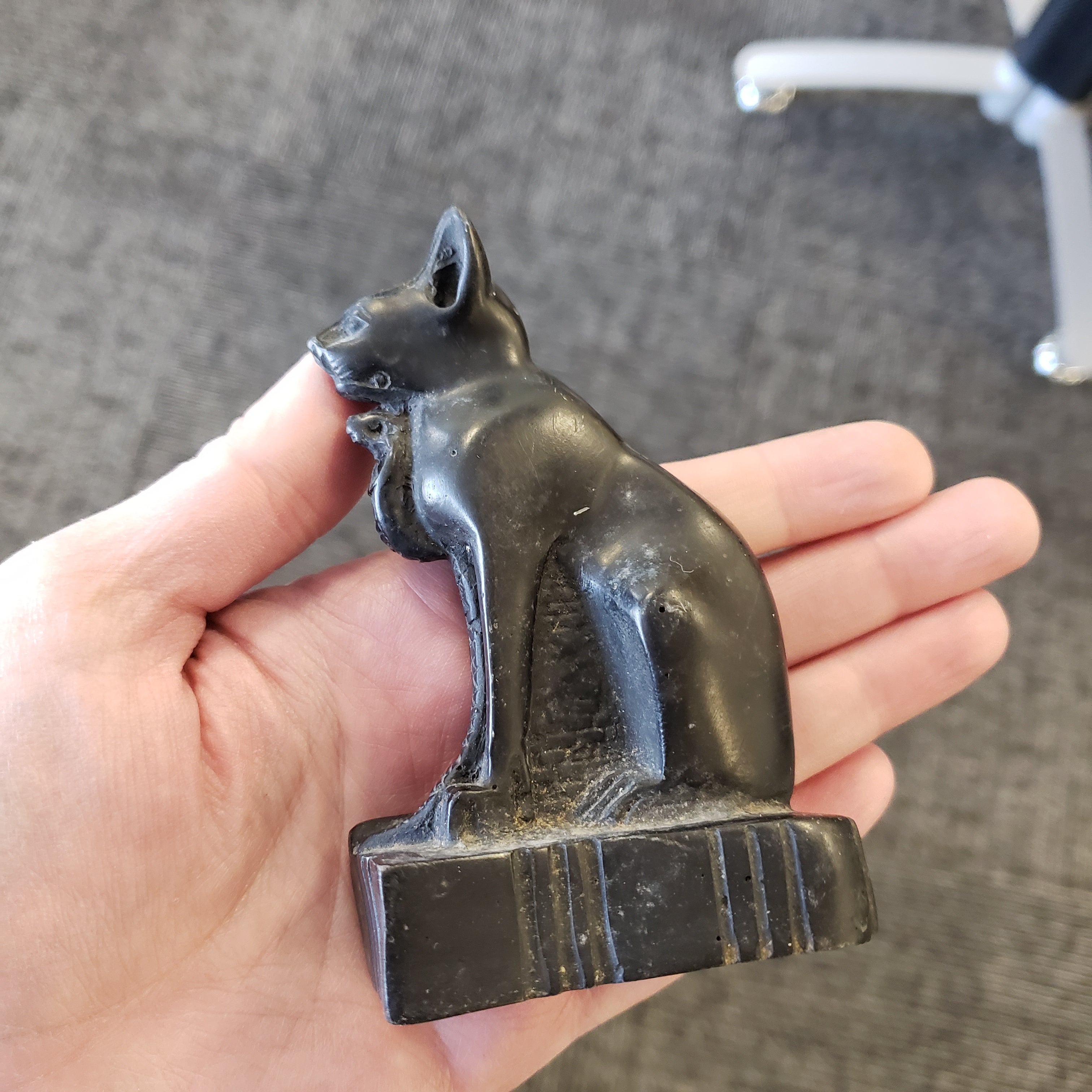 Hand holding a black cat statue with a detailed design on a gray carpeted floor.