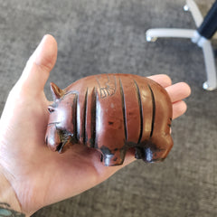 Hand holding a brown hippo statue on a carpeted floor.