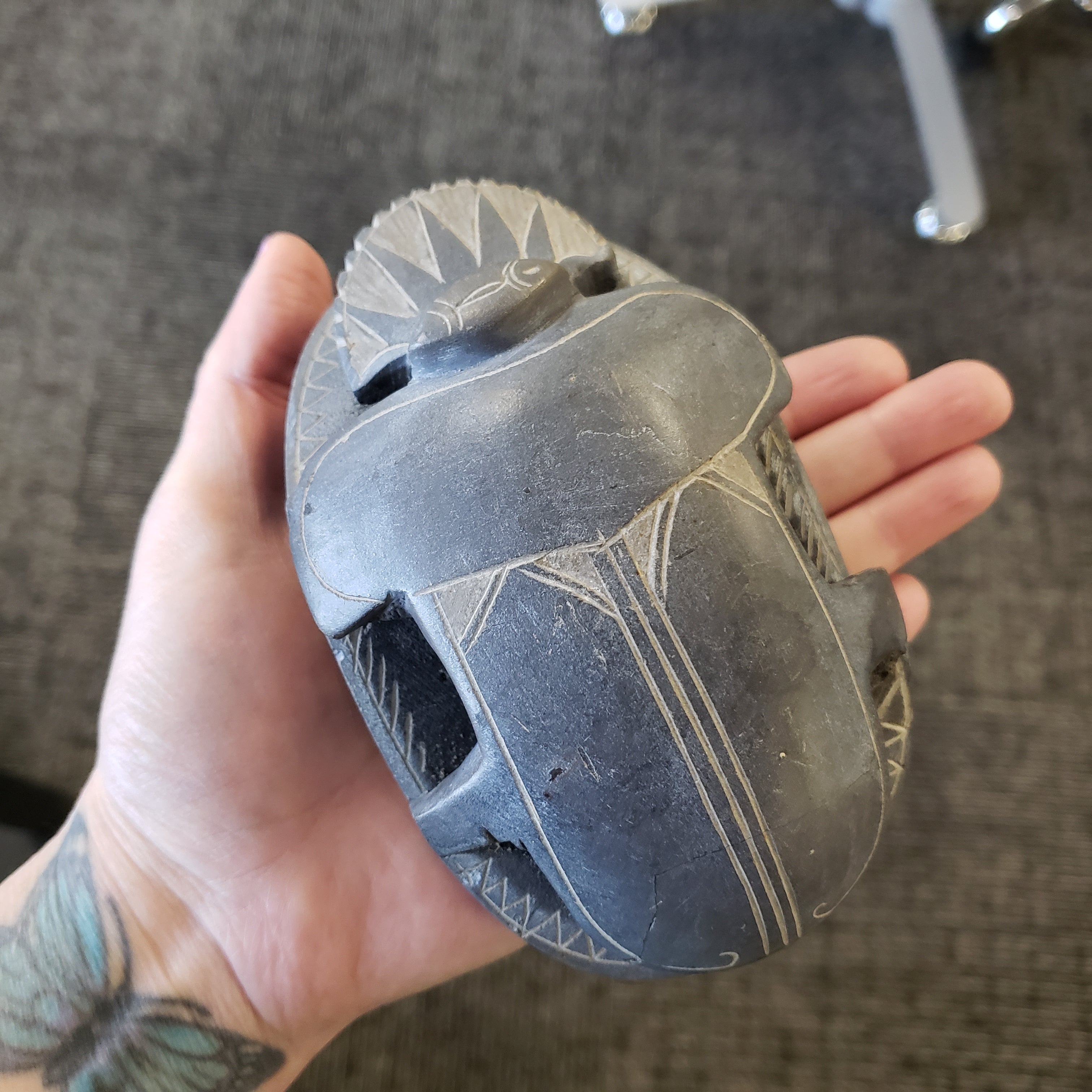 Hand holding a black stone sculpture of a scarab with carvings on a textured surface