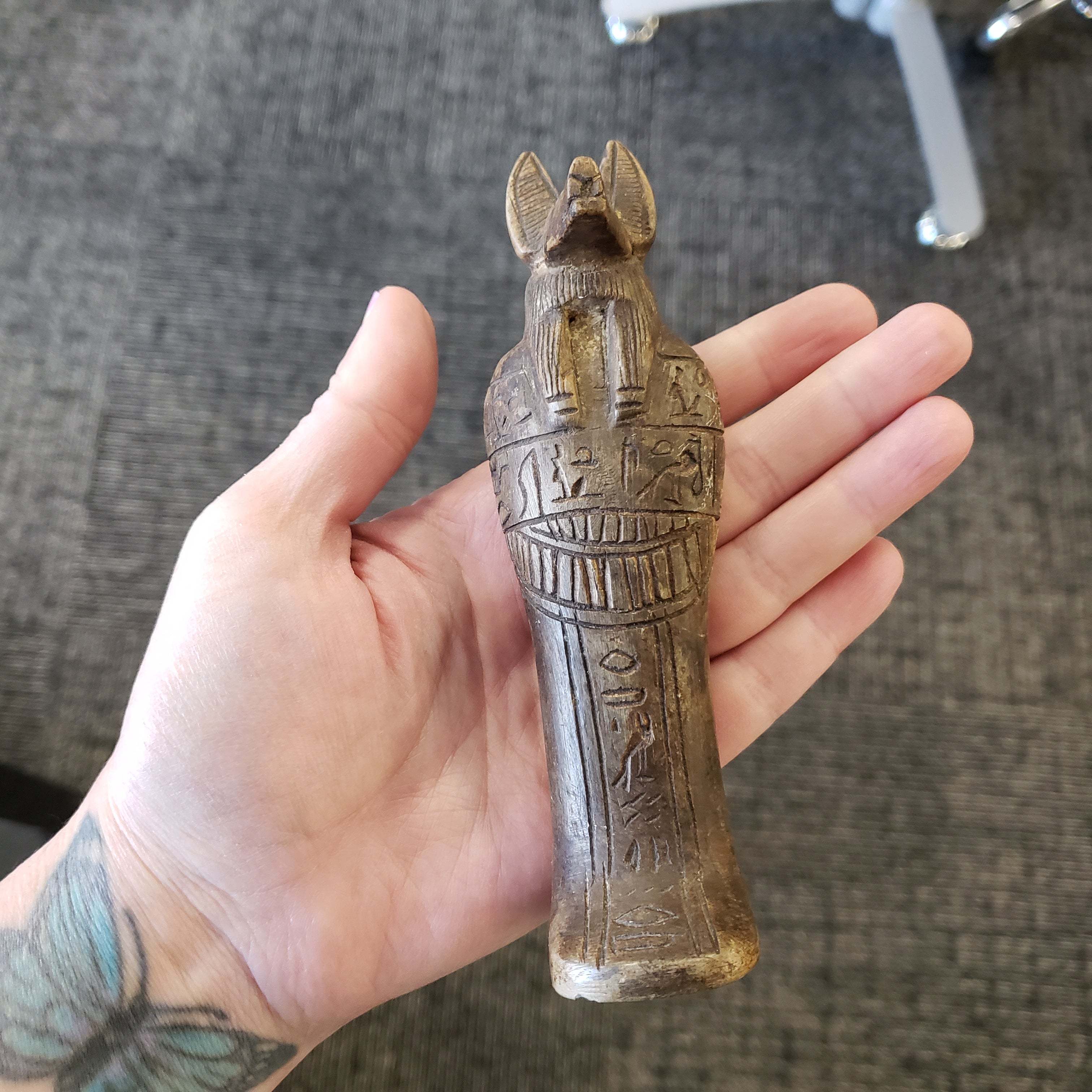Hand holding a small Egyptian-style amulet with hieroglyphics against a textured gray background