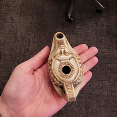 Hand holding a decorative oil lamp against a brown textured background