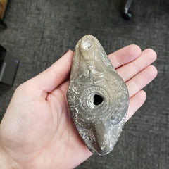 Hand holding a stone Egyptian goddess Hathor Oil Lamp with a worn surface against a dark textured background