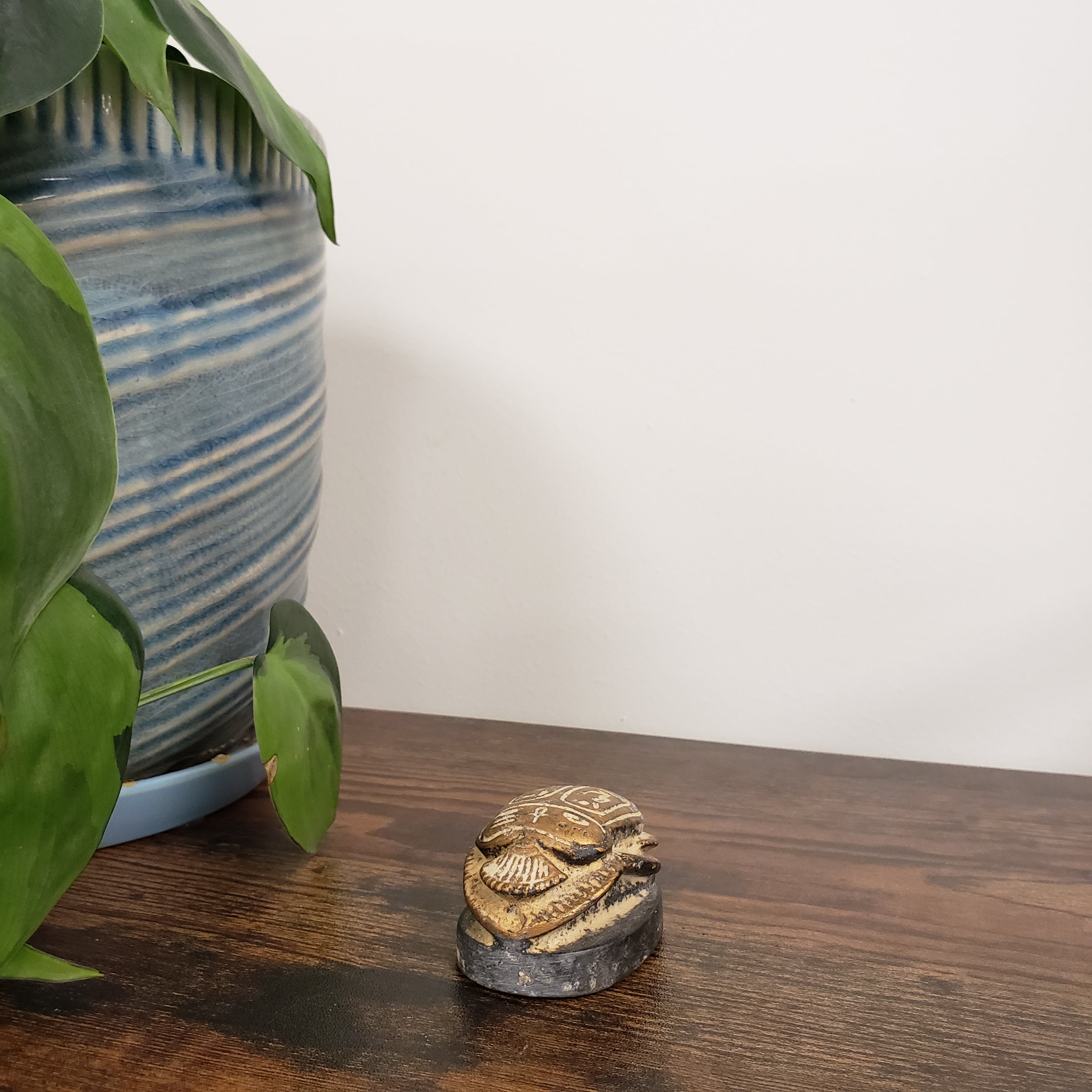 Decorative gold scarab statue on a wooden door with plants and striped fabric in the foreground.