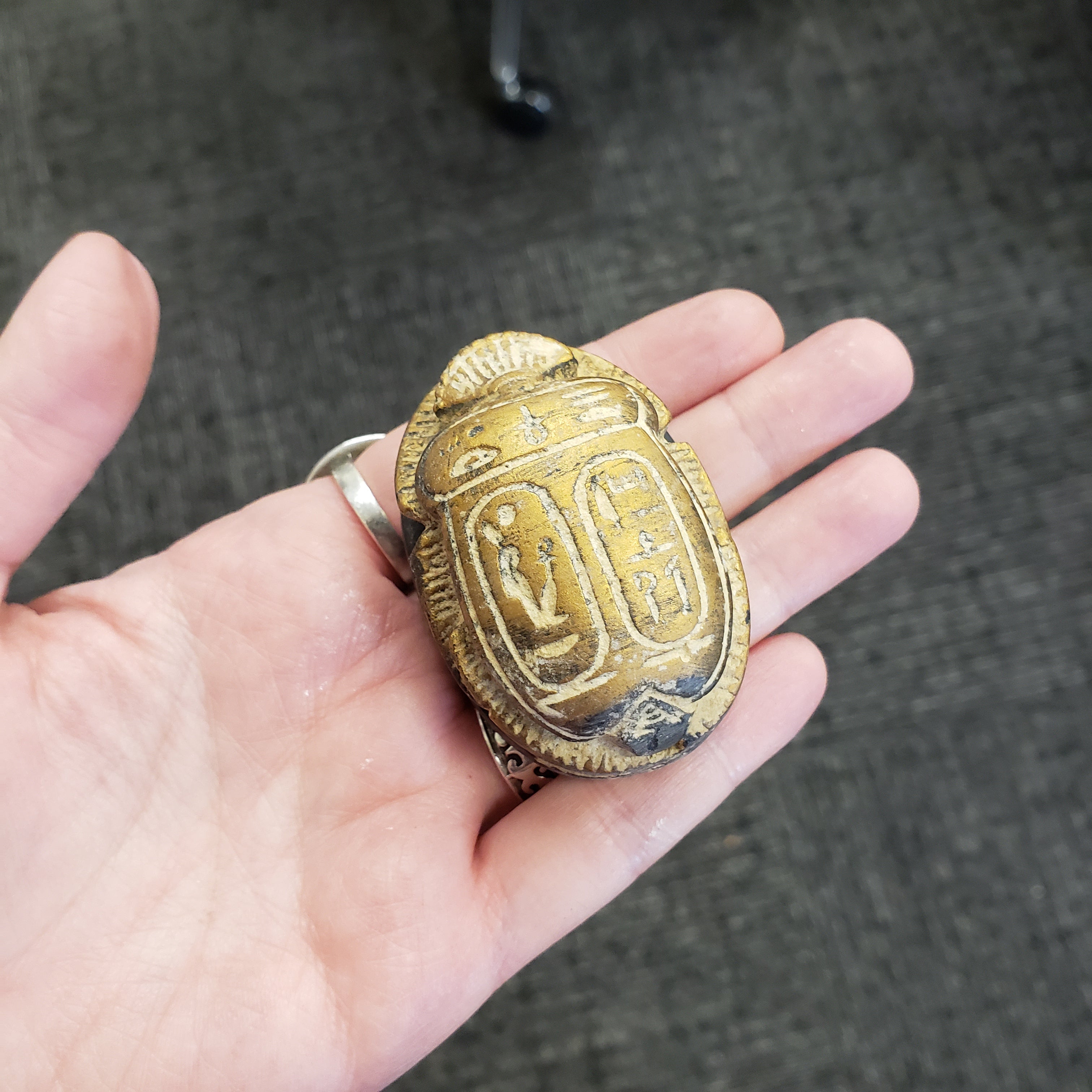 gold scarab statue with intricate designs held in a hand against a dark background