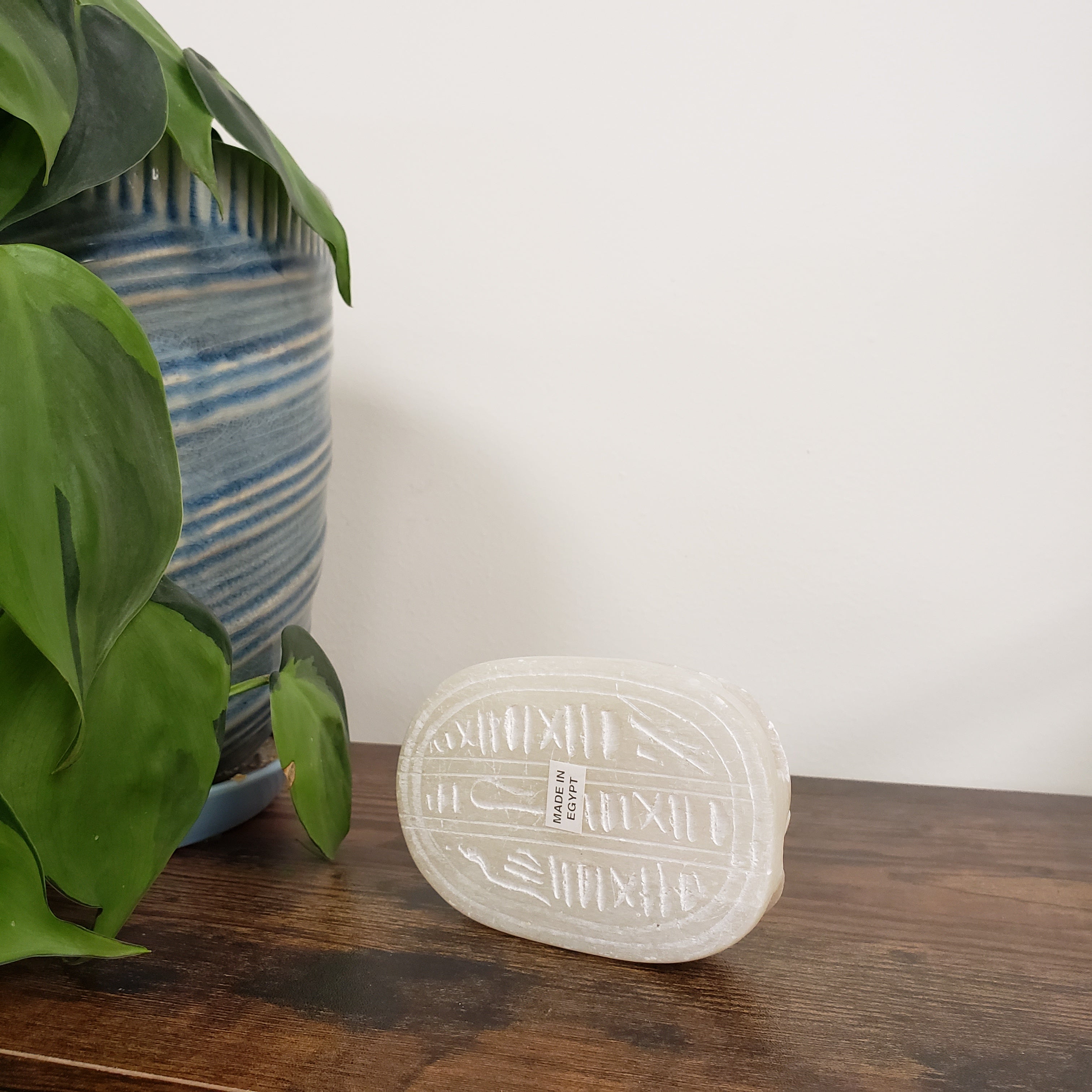 Decorative White soapstone scarab statue on a wooden surface next to green leaves.