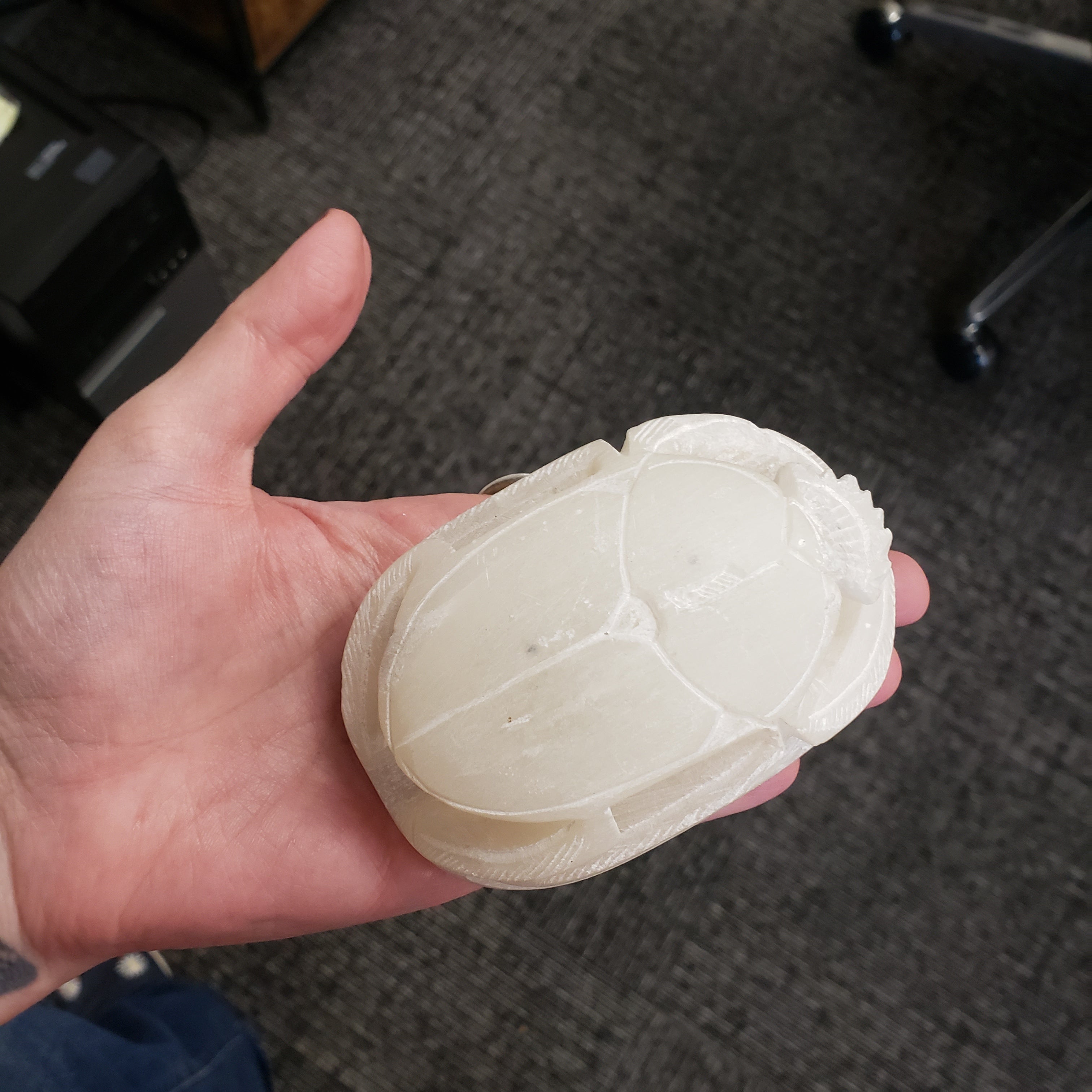 Hand holding a white soapstone scarab statue on a textured gray surface