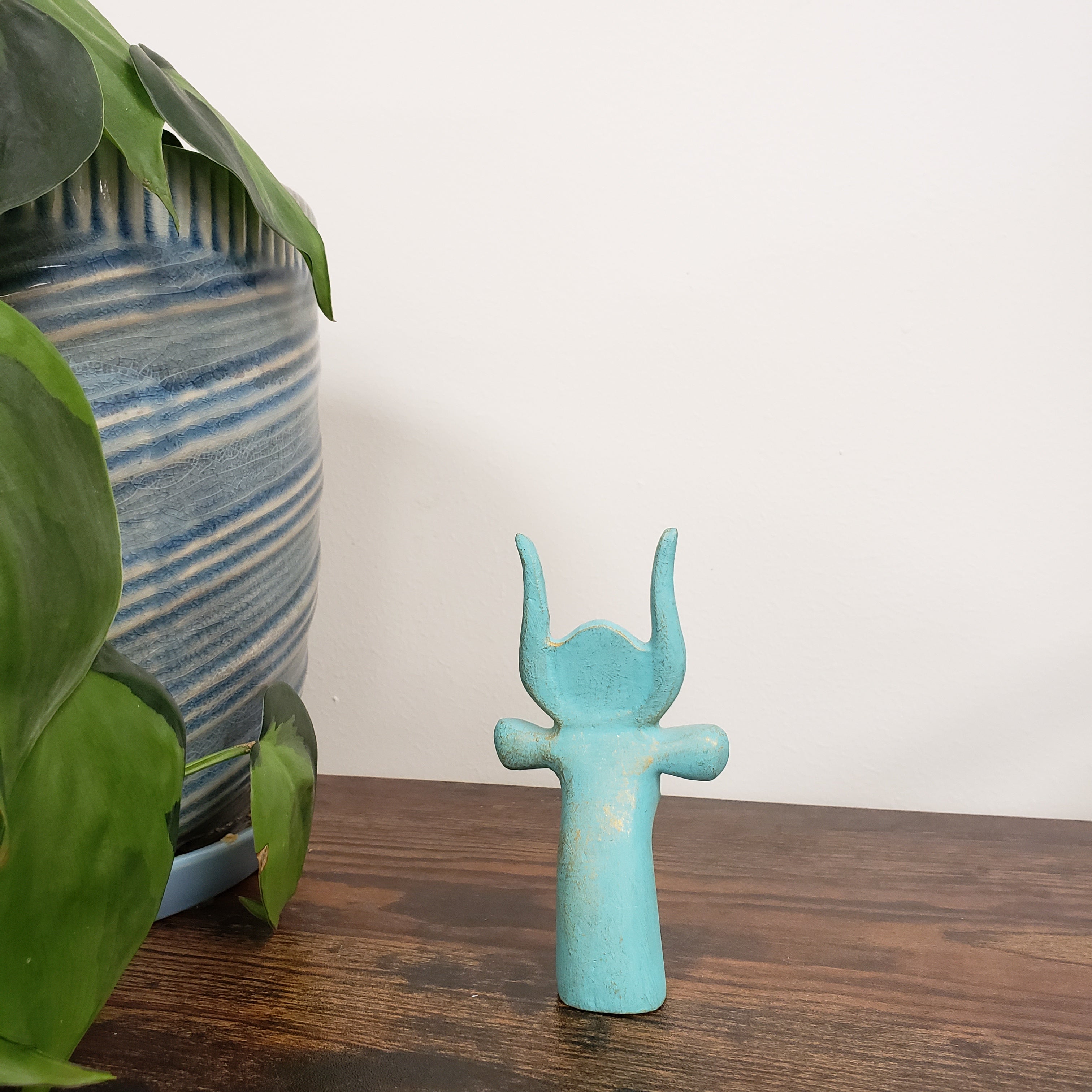 Turquoise Egyptian goddess Hathor bust statue on a wooden surface with plants and striped fabric in the background