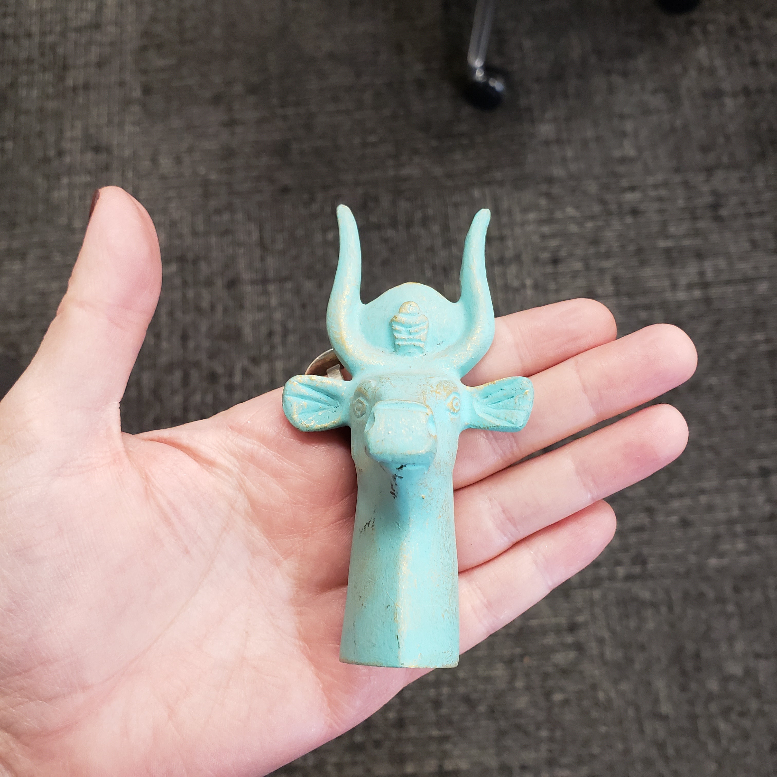 Turquoise decorative item held in a hand against a textured gray background