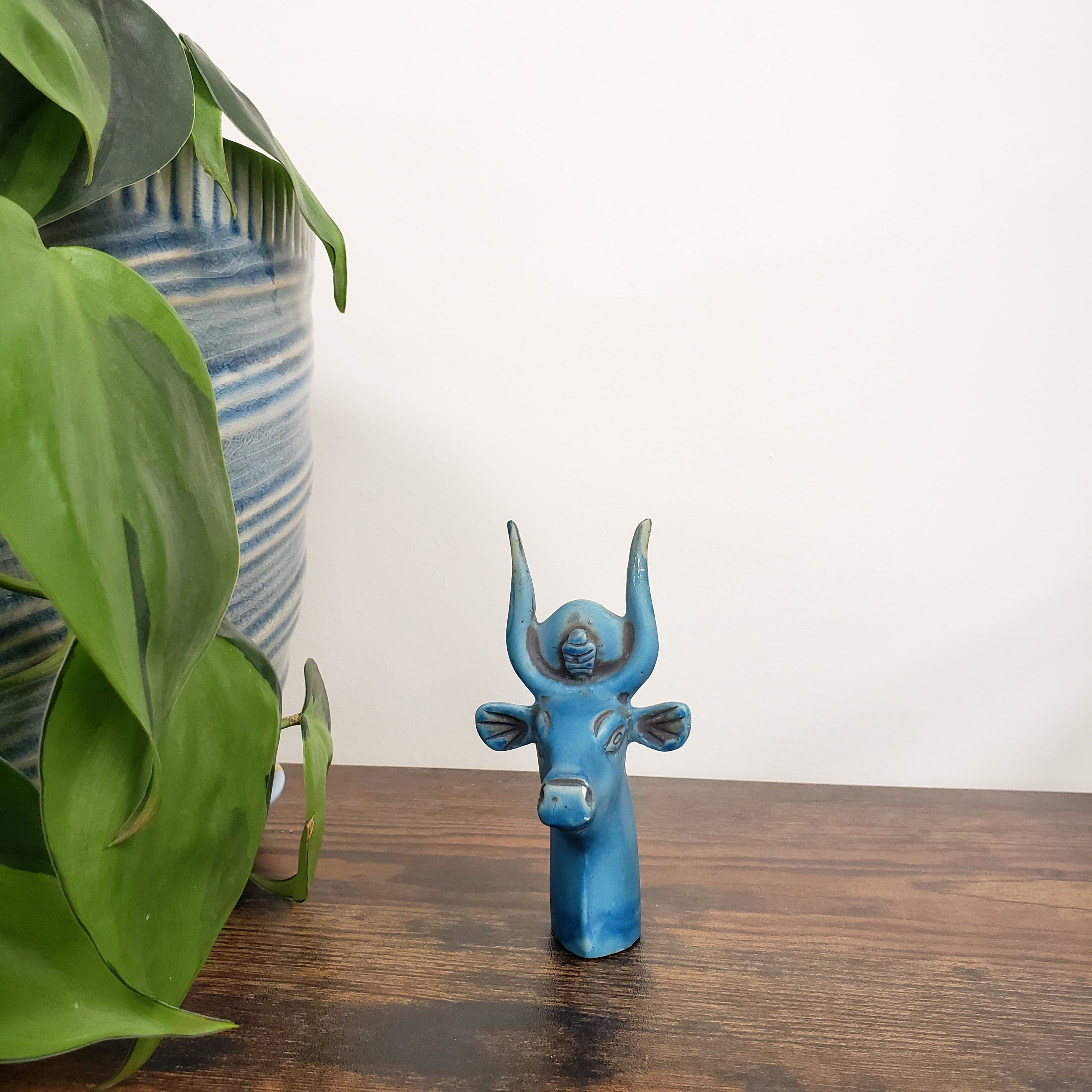 Blue Egyptian goddess Hathor bust statue on a wooden surface with green leaves in the foreground