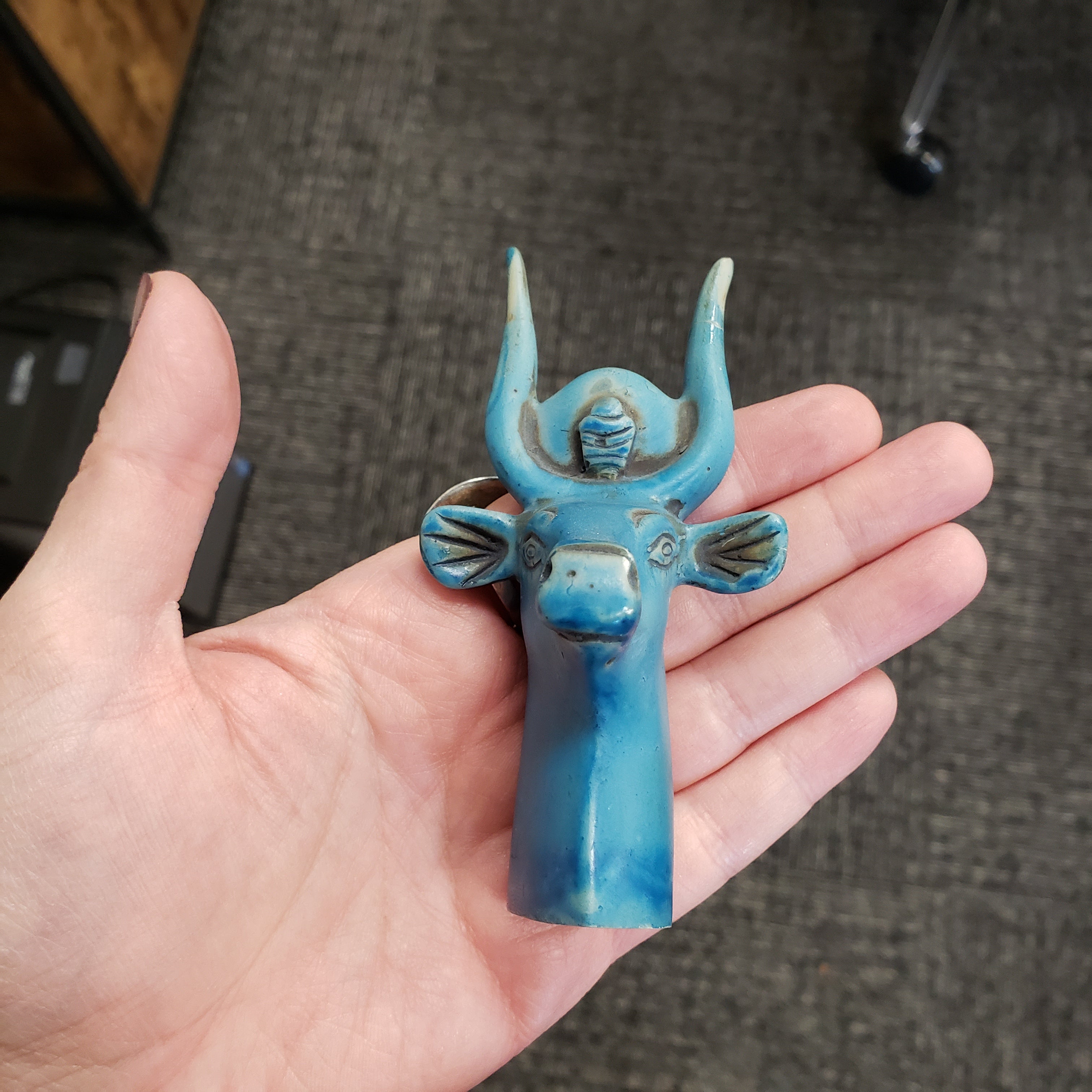 Hand holding a blue Egyptian goddess Hathor bust statue with decorative elements against a blurred background