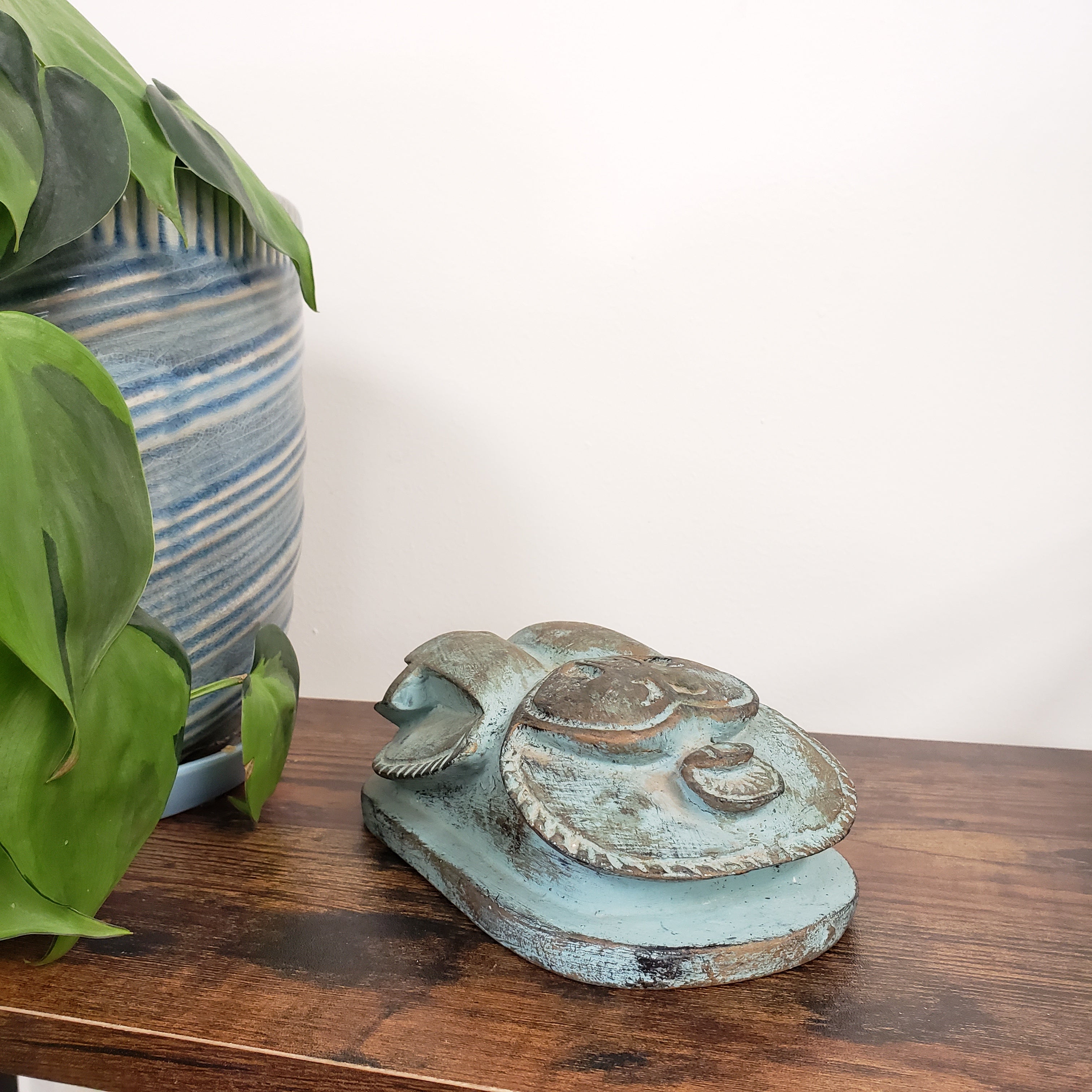 Decorative Egyptian scarab statue with a wooden board and plants in the background
