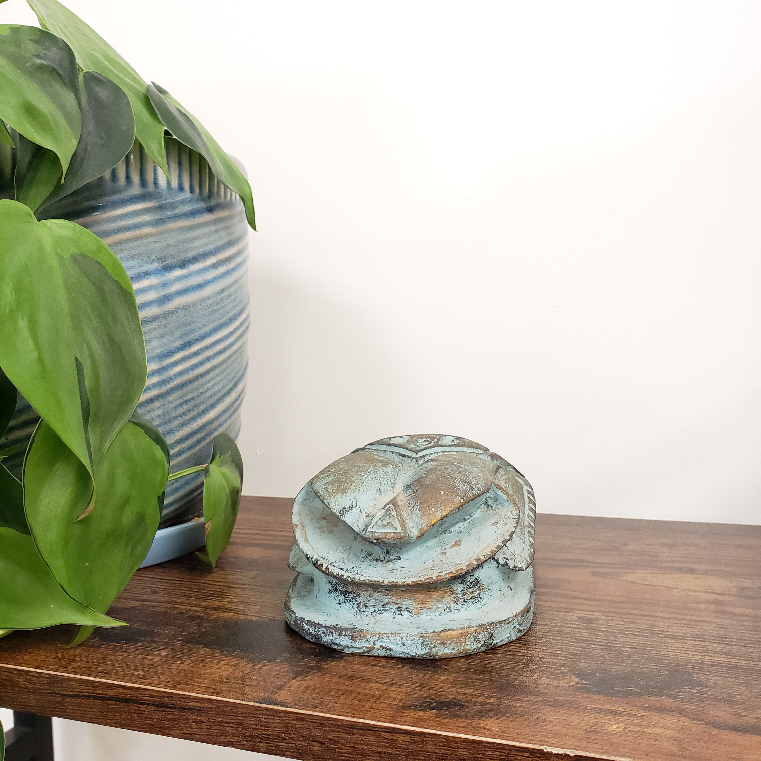 Decorative Egyptian scarab statue with a plant and striped fabric in the background