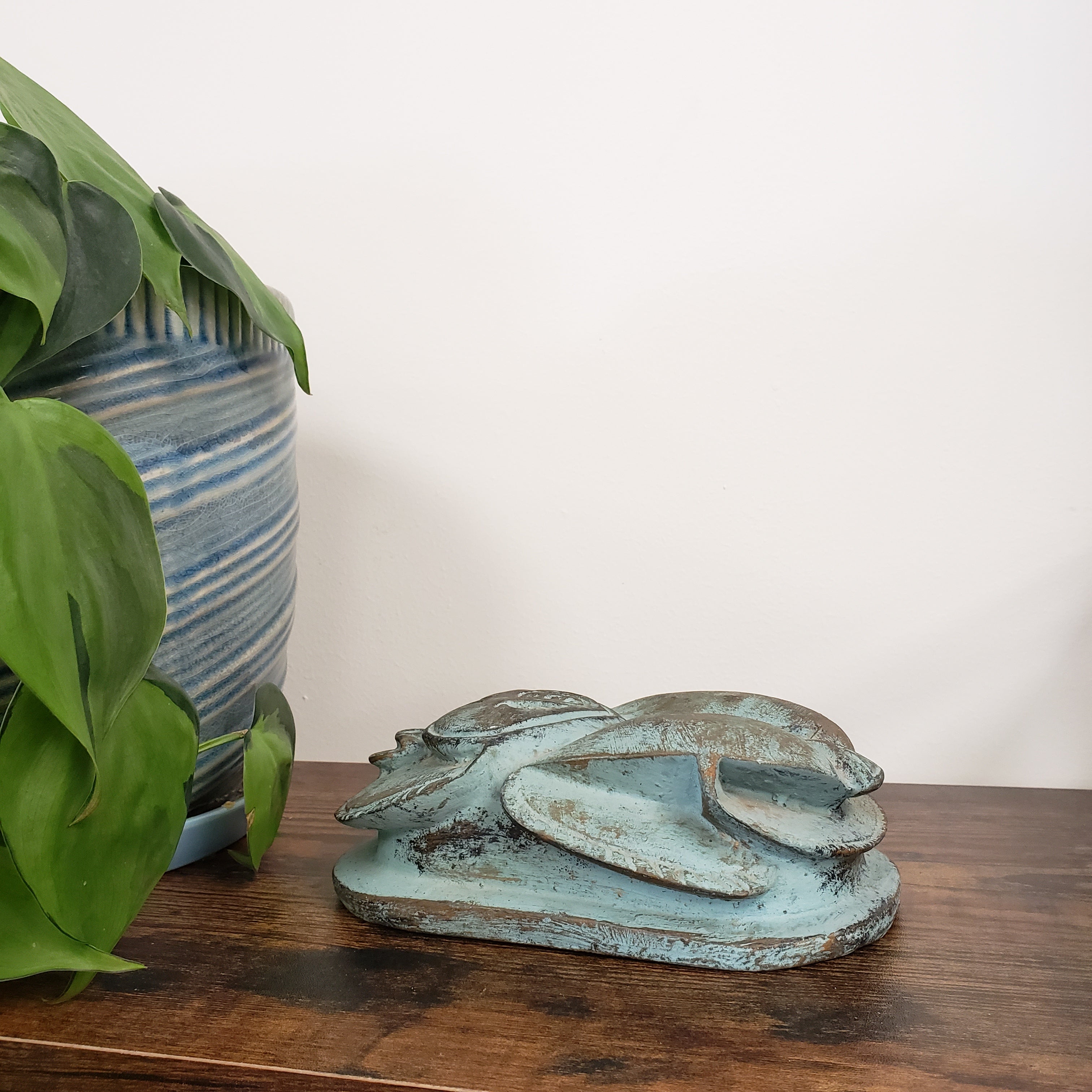 Decorative Egyptian scarab statue on a wooden board with plants and striped fabric in the background