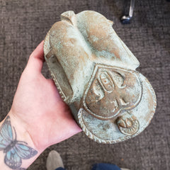 Hand holding a stone sculpture of Egyptian scarab statue on a textured surface.