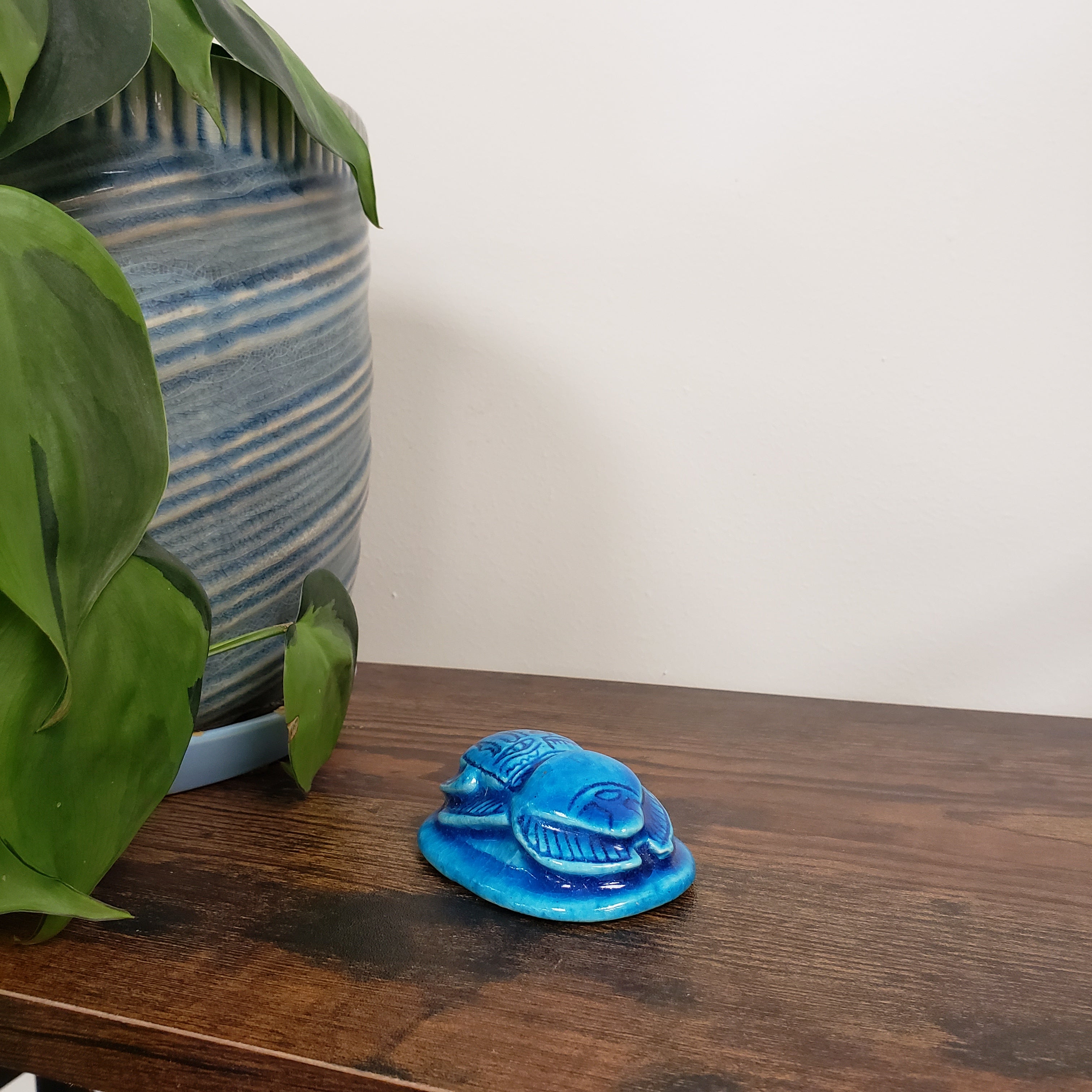 Blue decorative item on a wooden surface with green leaves and a striped fabric in the background