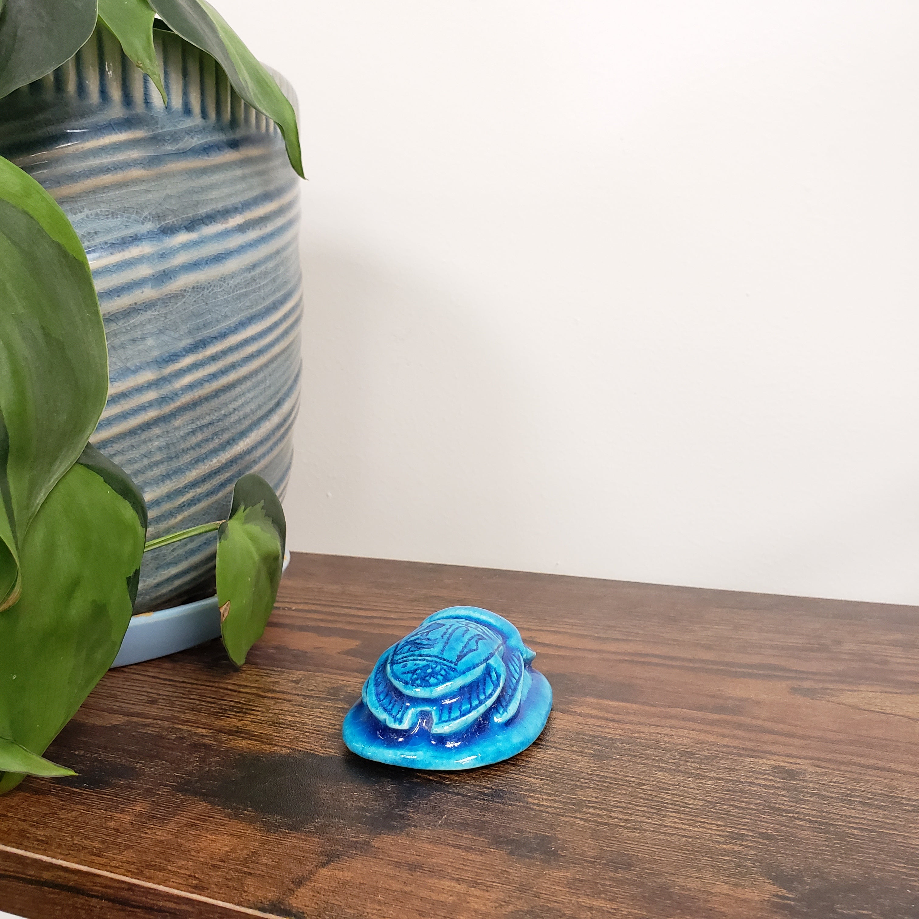 Blue decorative item on a wooden surface with green leaves and a striped fabric in the background