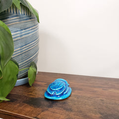 Blue decorative item on a wooden surface with green leaves and a striped fabric in the background