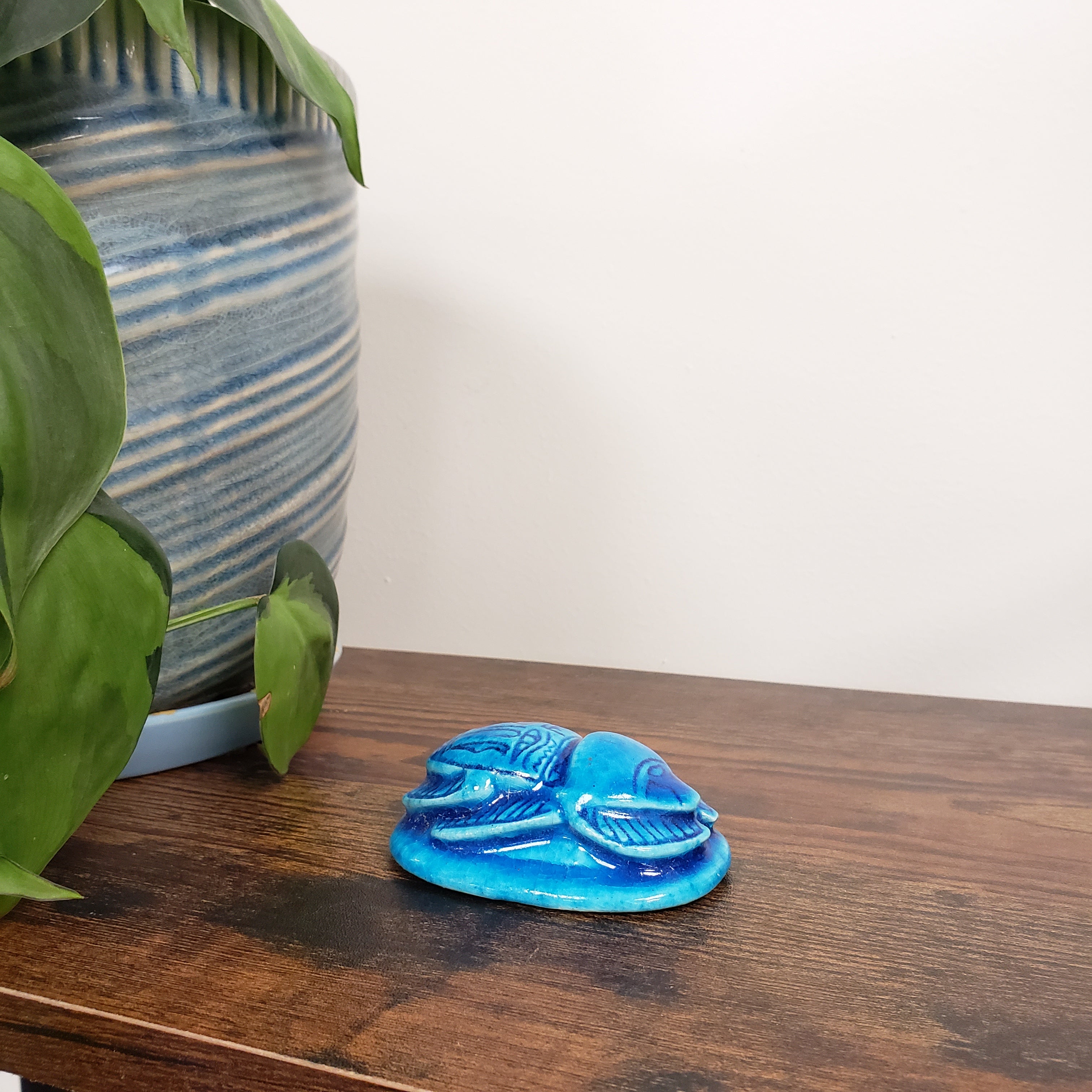 Blue decorative item on a wooden surface with green leaves in the foreground