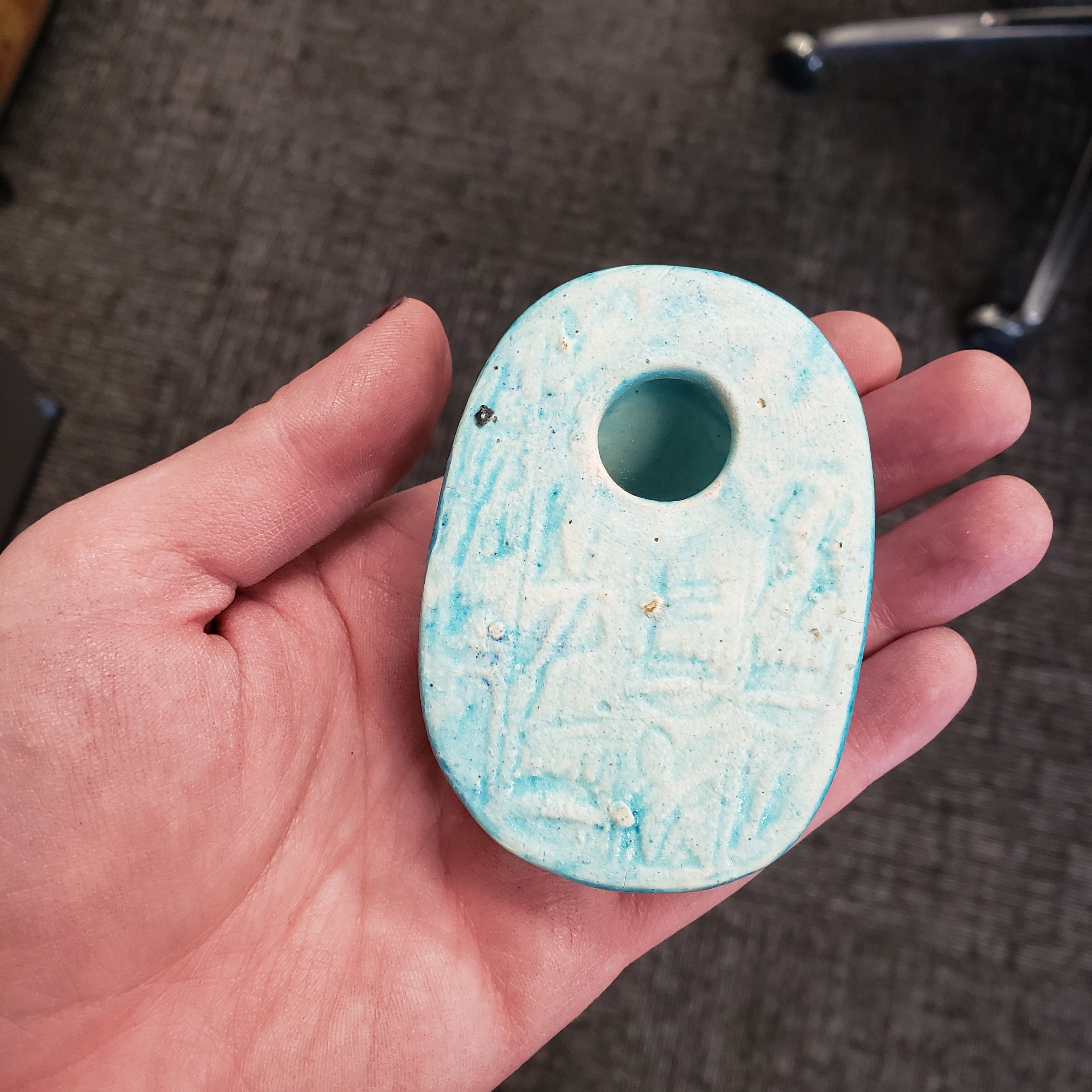 Hand holding a blue and white textured stone with a central hole.