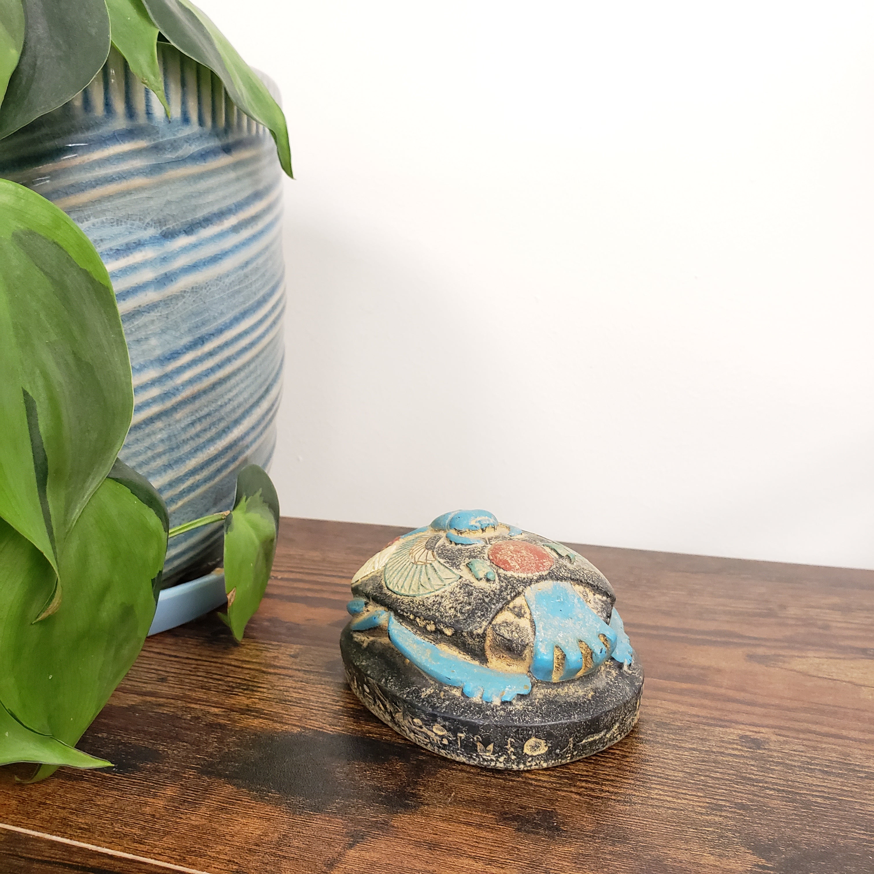 Decorative Egyptian scarab statue on a wooden board, surrounded by green leaves.