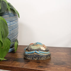 Decorative Egyptian scarab statue on a wooden panel with plants and striped fabric in the background