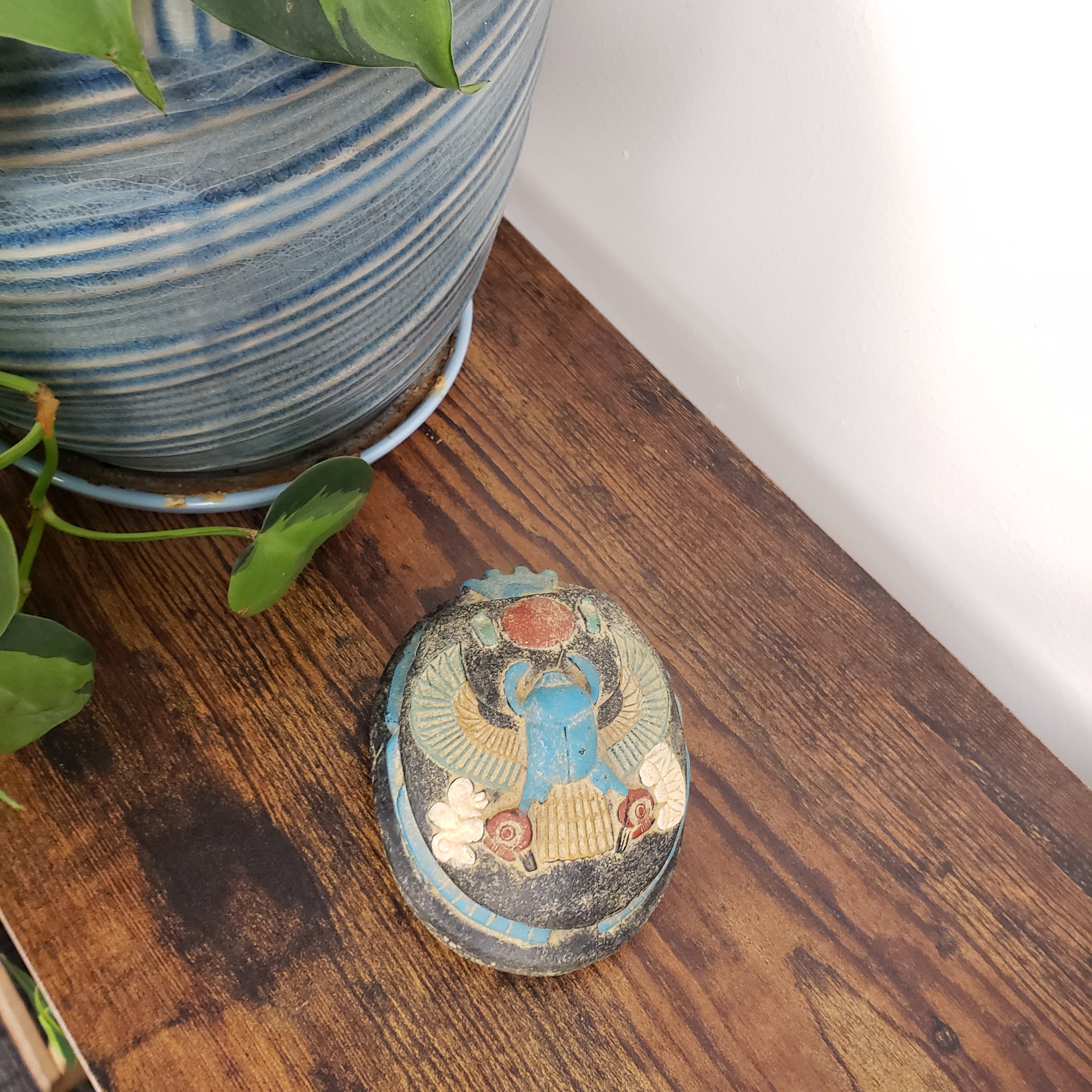 Decorative Egyptian scarab statue on a wooden surface next to a plant