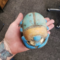 Hand holding a decorative object with blue and gold colors on a textured surface.