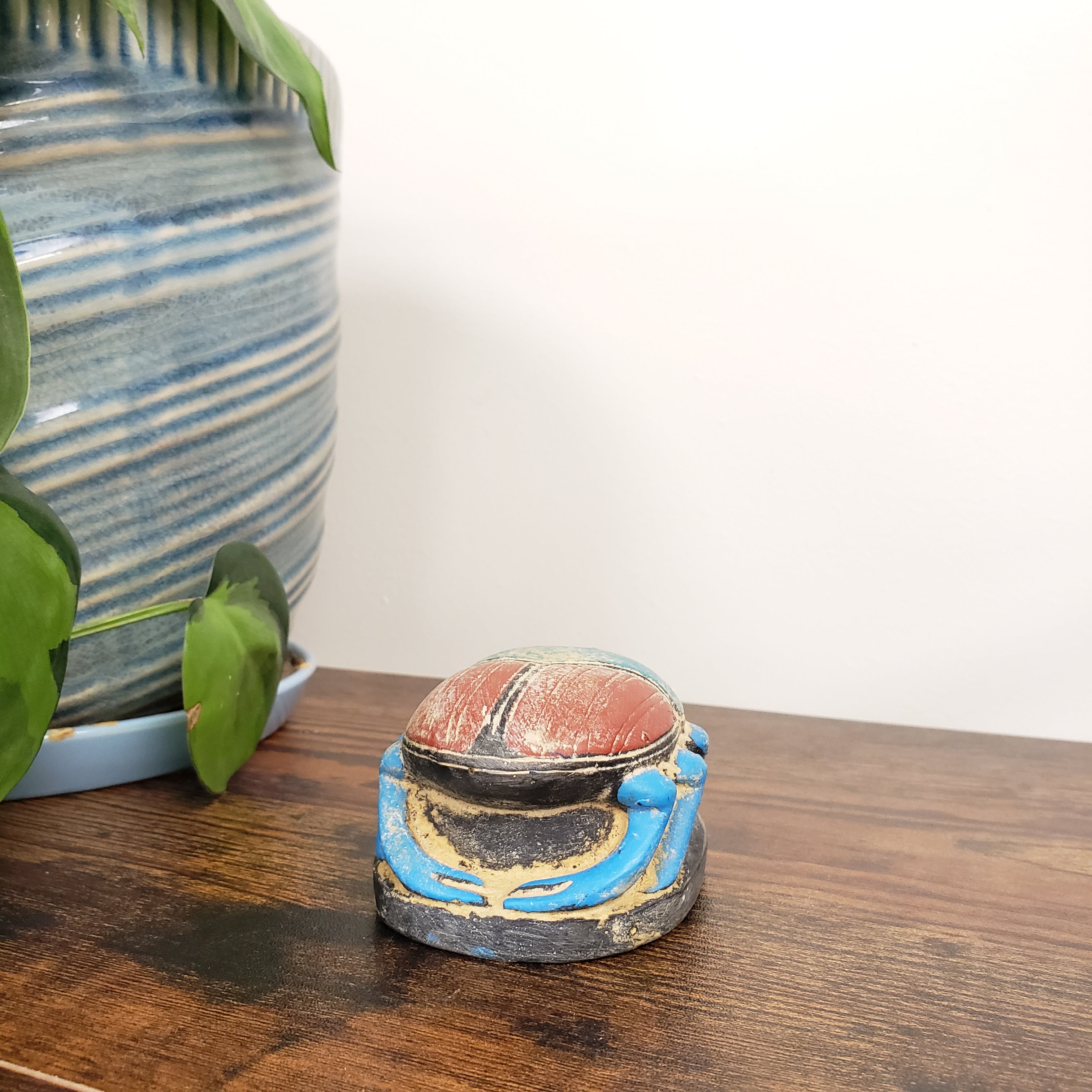 Decorative Egyptian scarab statue with a striped vase and plant leaves in the background