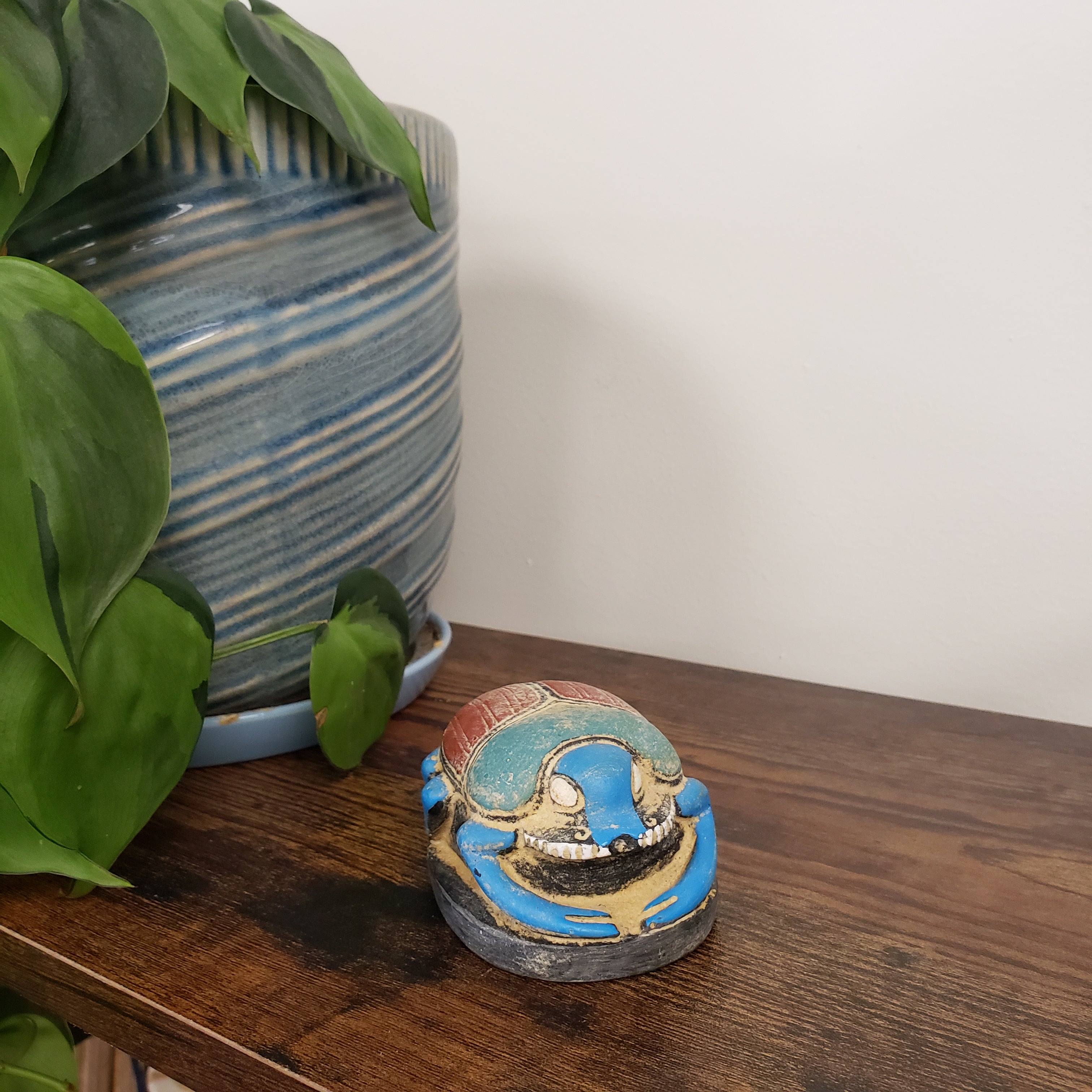Decorative Egyptian scarab statue on a wooden surface with a plant in the background