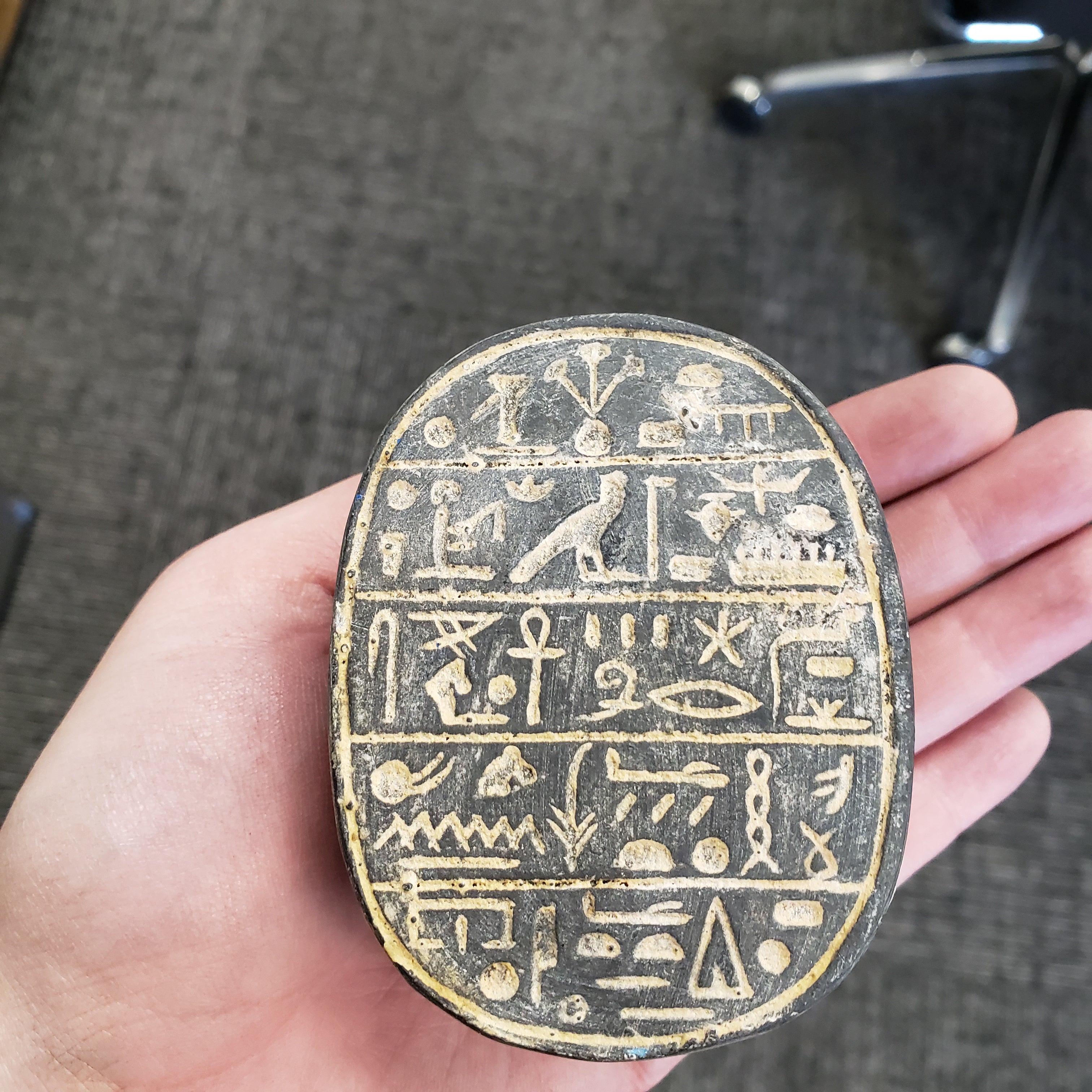 Hand holding a circular object with hieroglyphics on a textured surface
