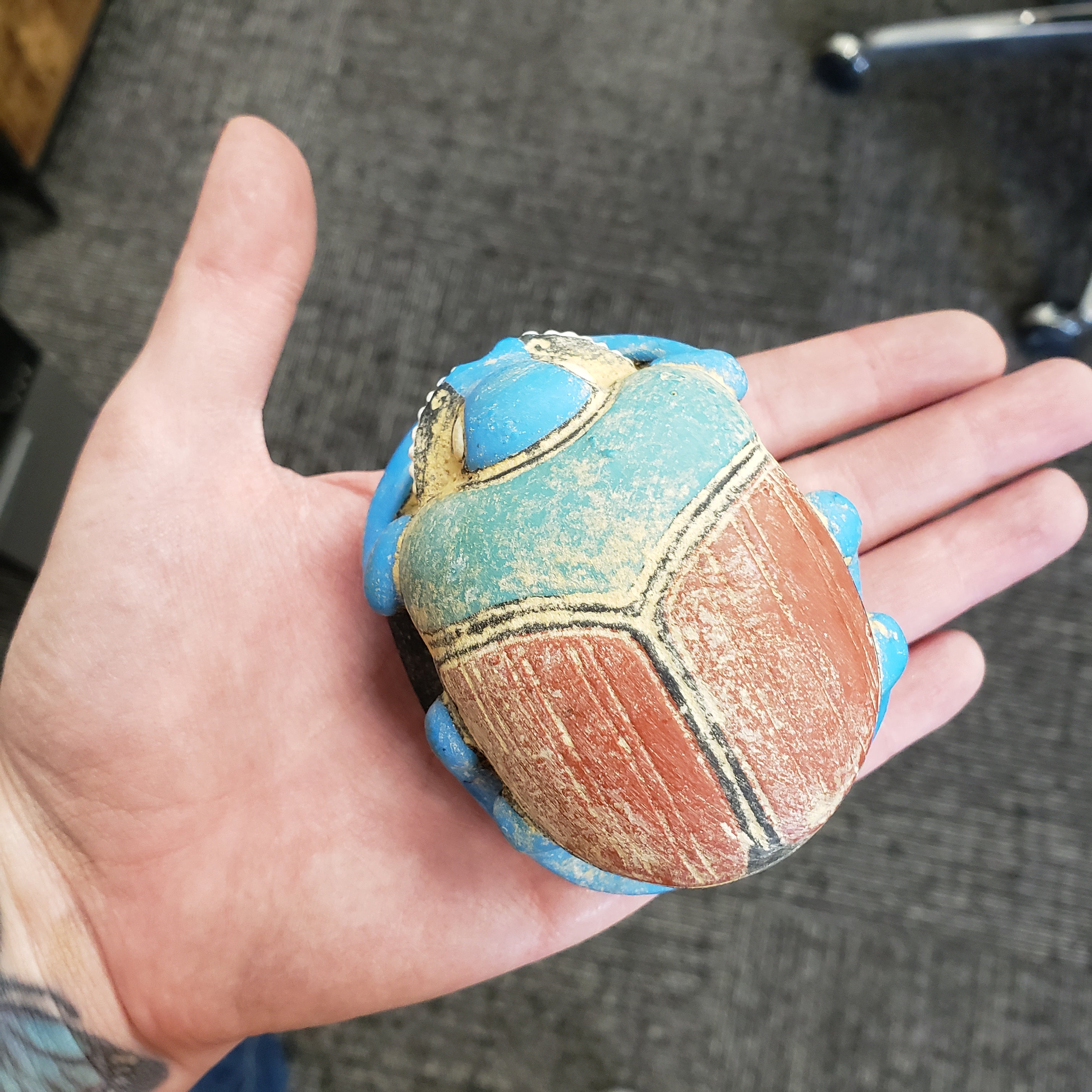 Hand holding a textured, multicolored stone with geometric patterns on a gray surface.