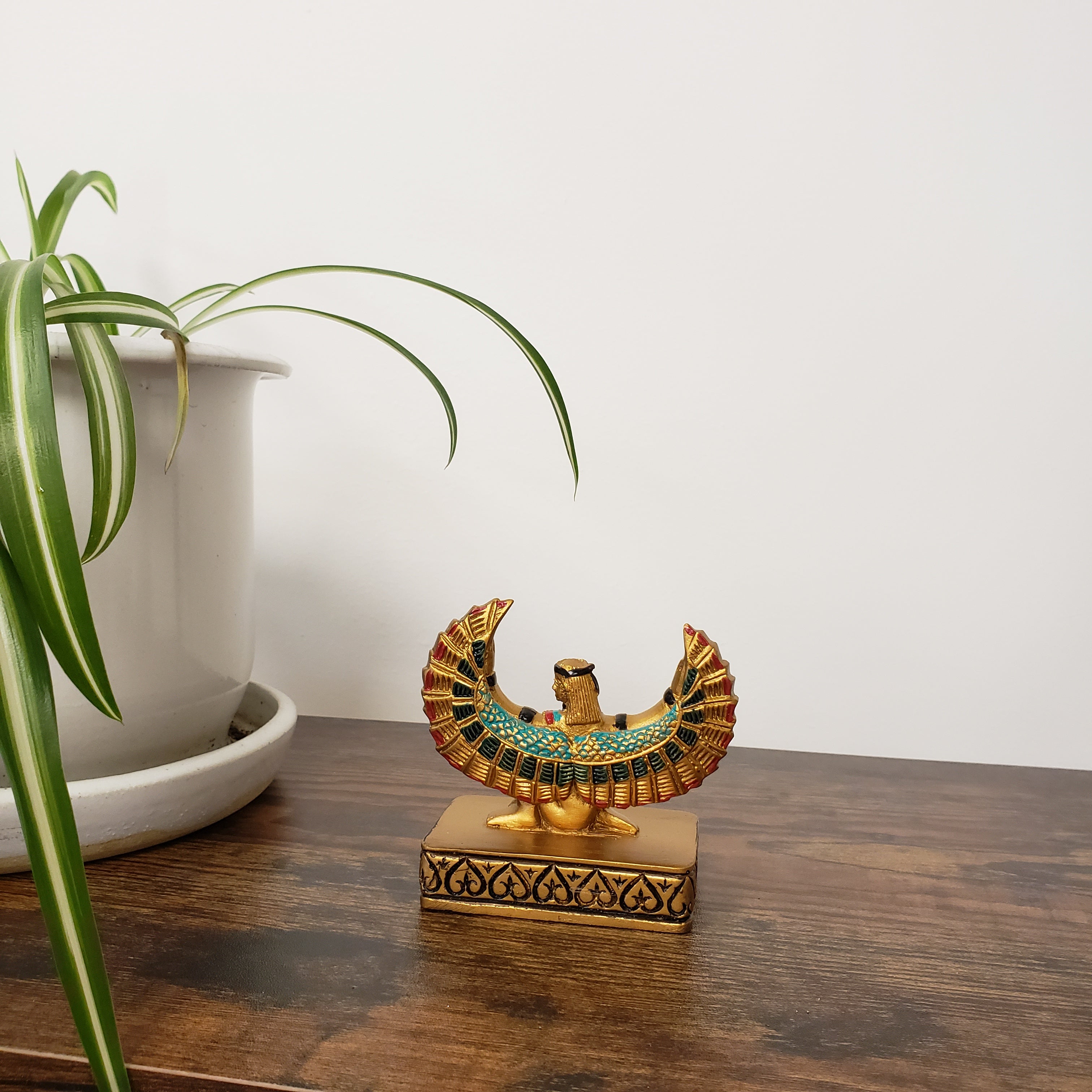 Decorative statue with Egyptian-style design on a wooden surface with a plant in the foreground.