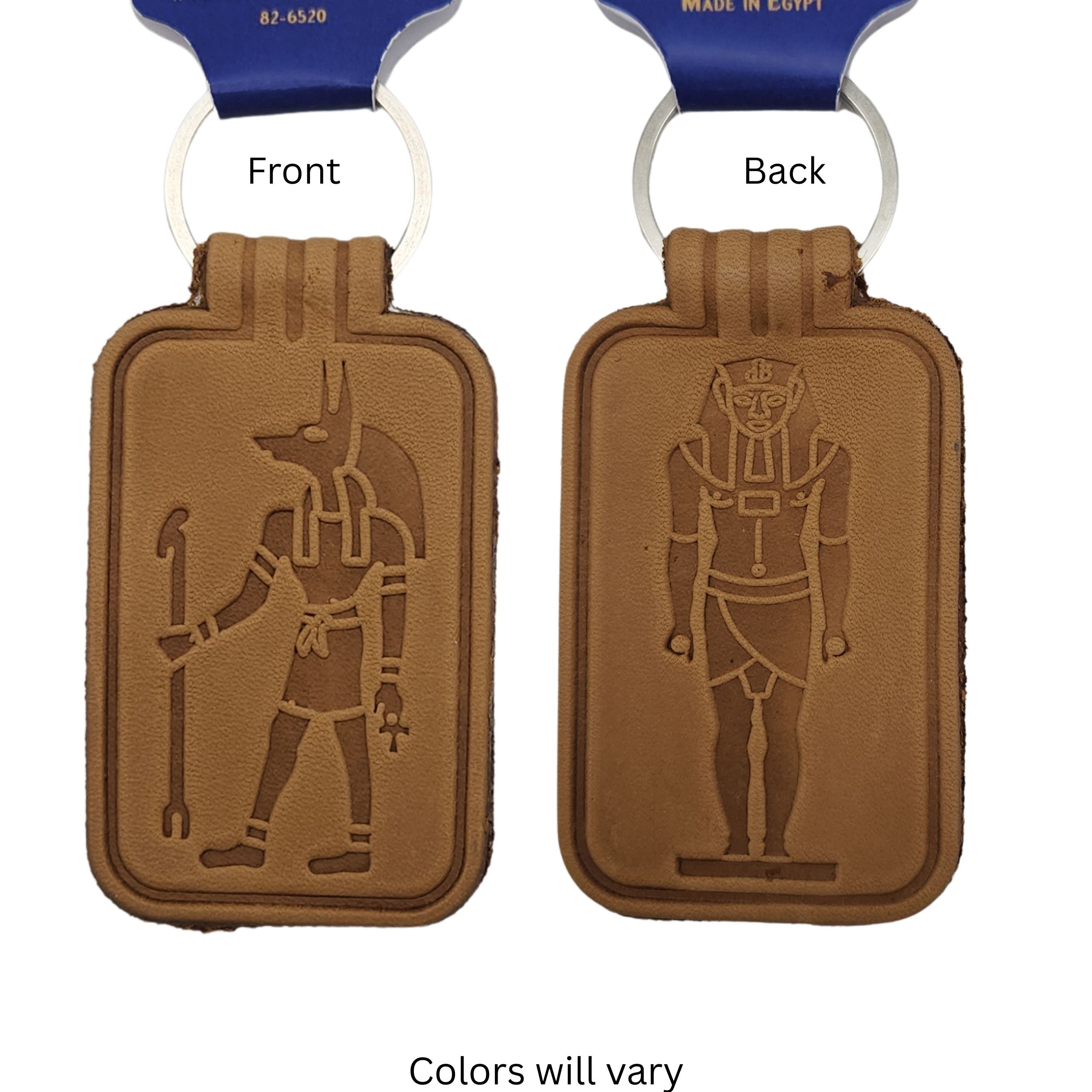 One tan leather keychains shown  Front and Back, each with a white key loop. The front side features an embossed Anubis figure, and the back side features a pharaoh figure.