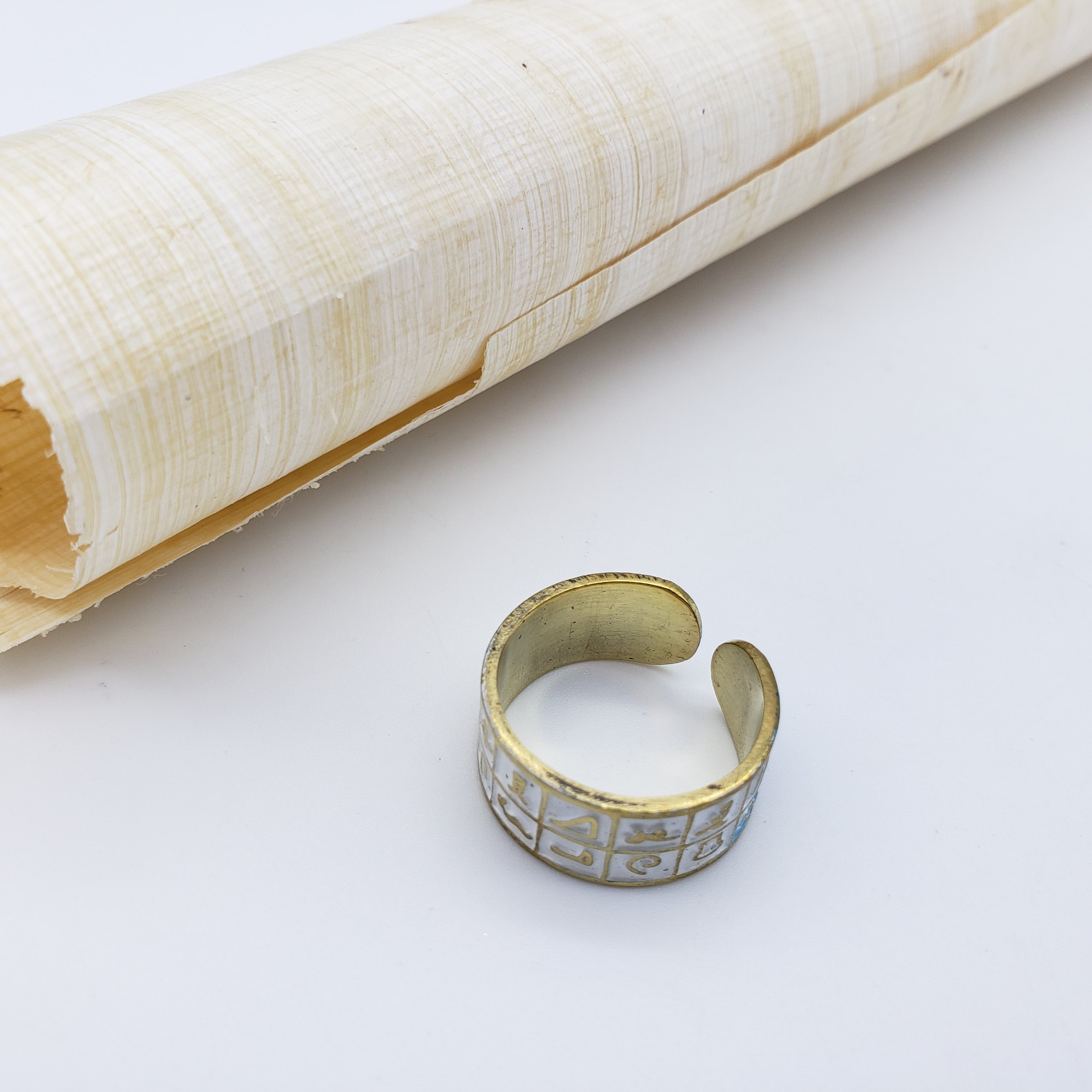 Gold ring with intricate design on a white surface next to a rolled-up piece of paper.