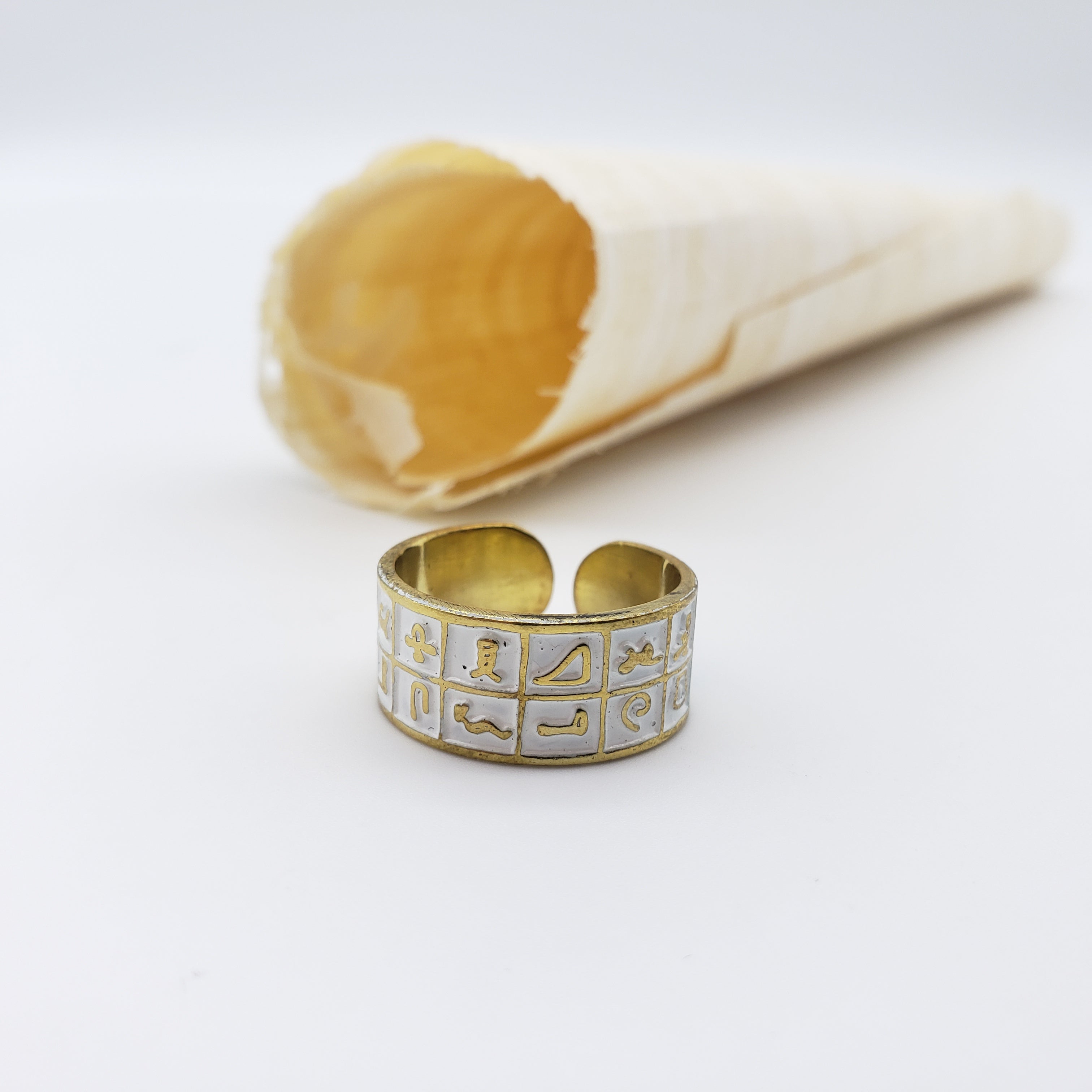 Gold ring with hieroglyphic design next to a white shell on a light gray background