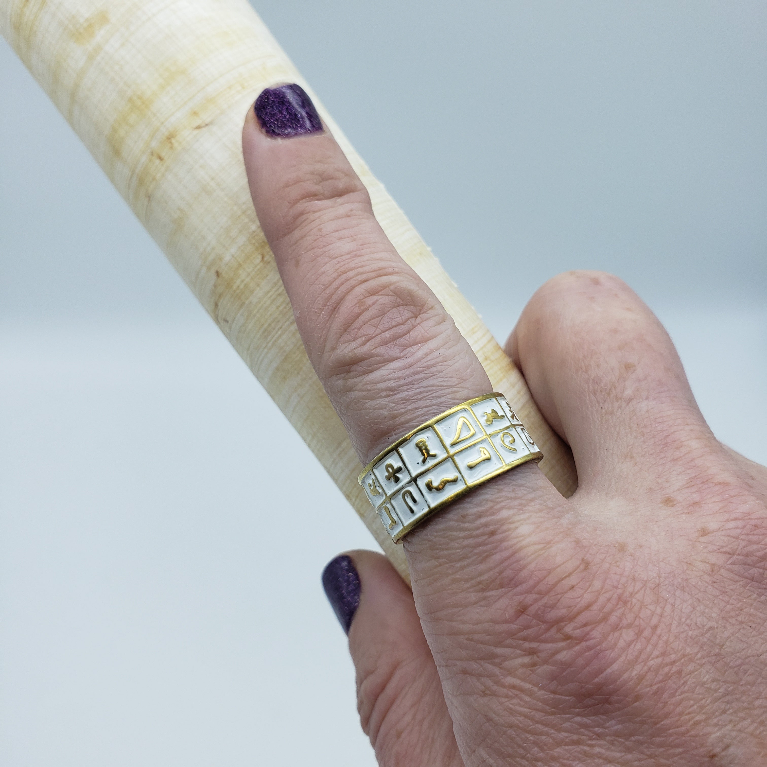 Hand wearing a gold ring with symbols holding a wooden object against a light background