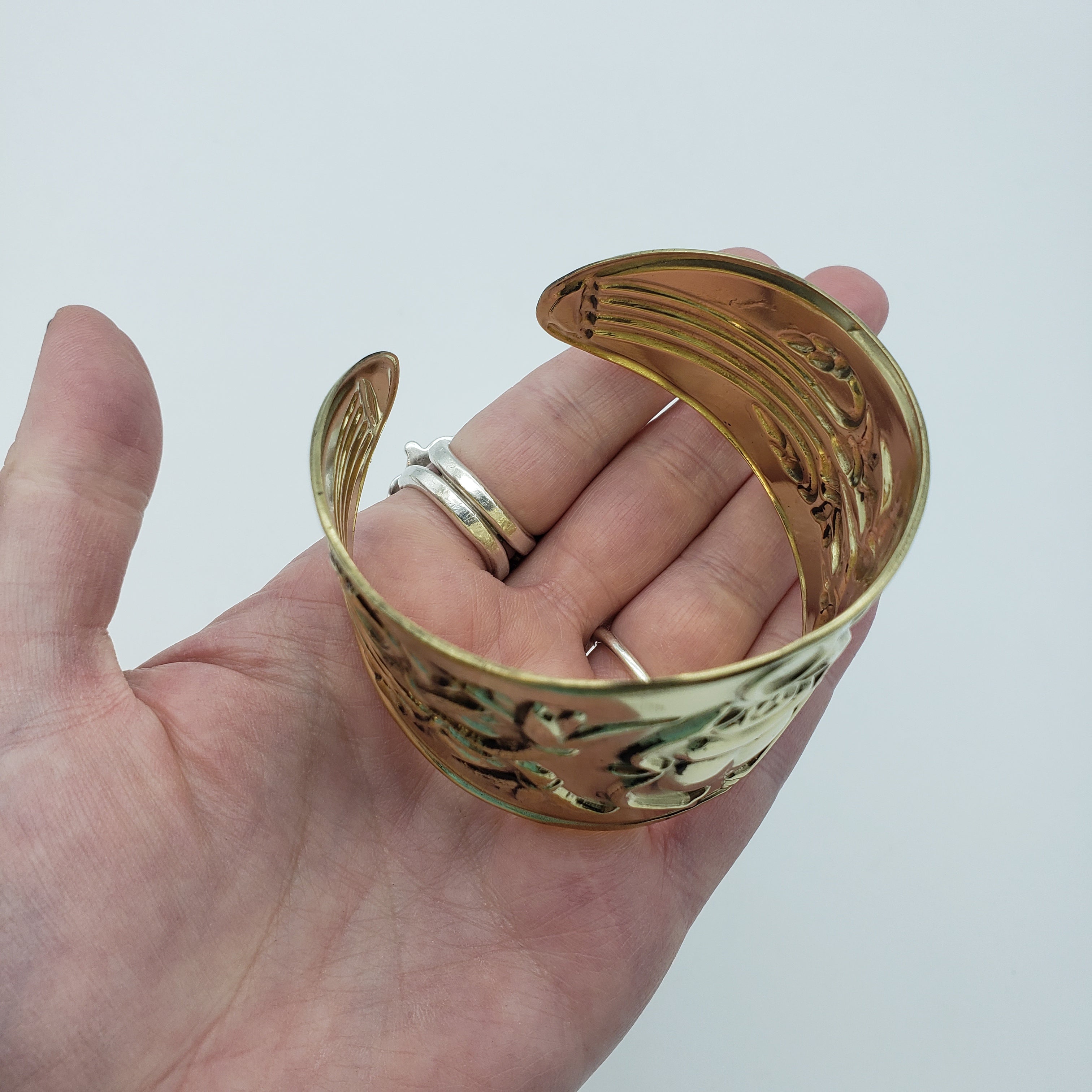 Gold bracelet being held by a hand on a white background