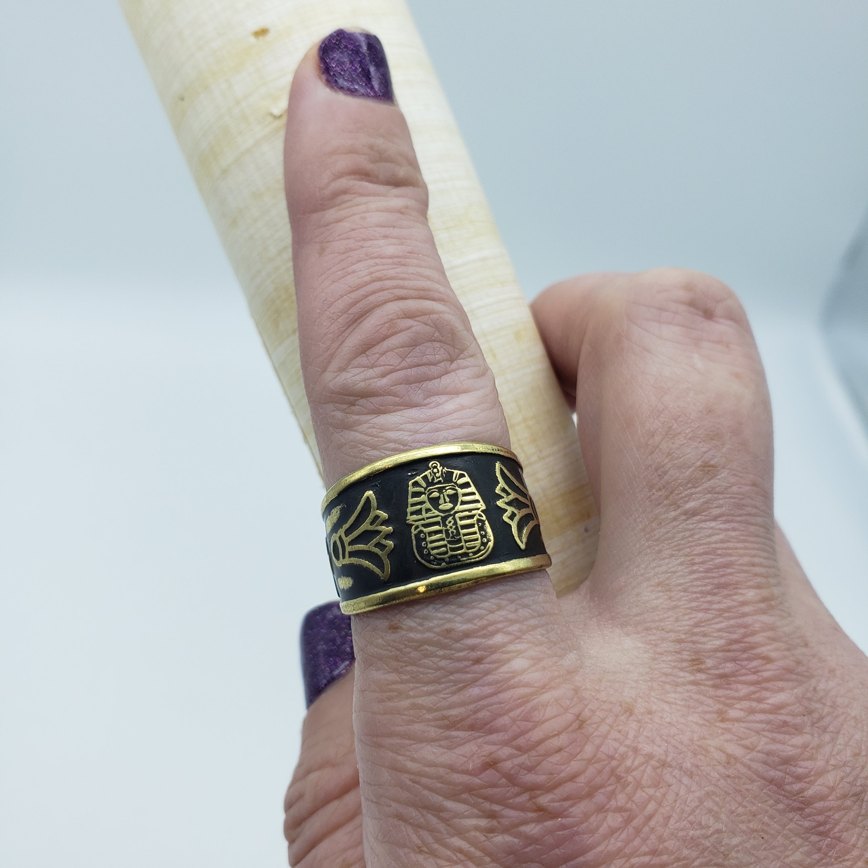 Gold ring with intricate design on a finger against a white background