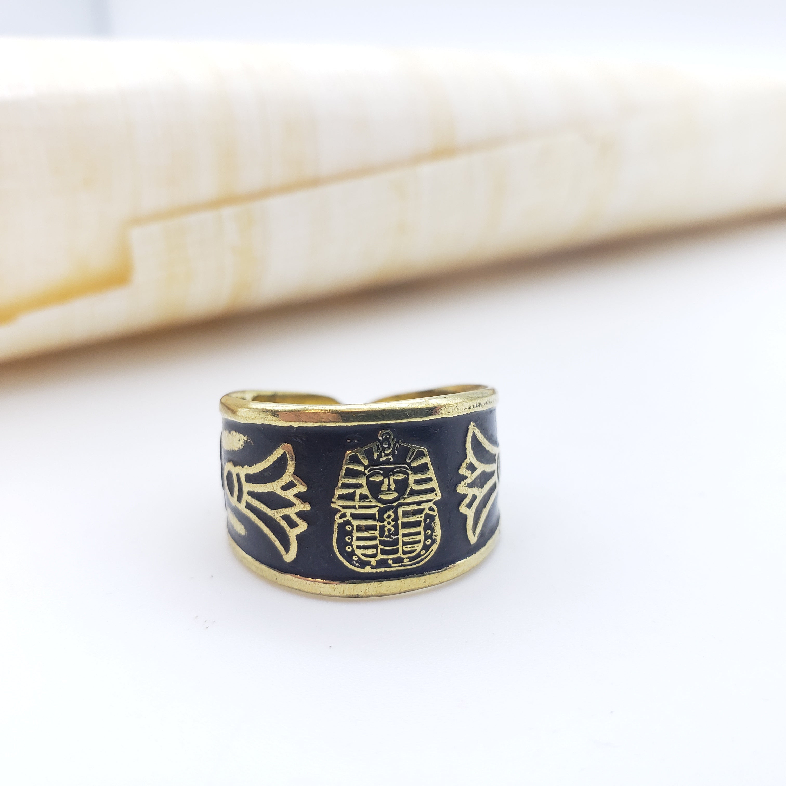 Black ring with gold pharaoh design on a white surface