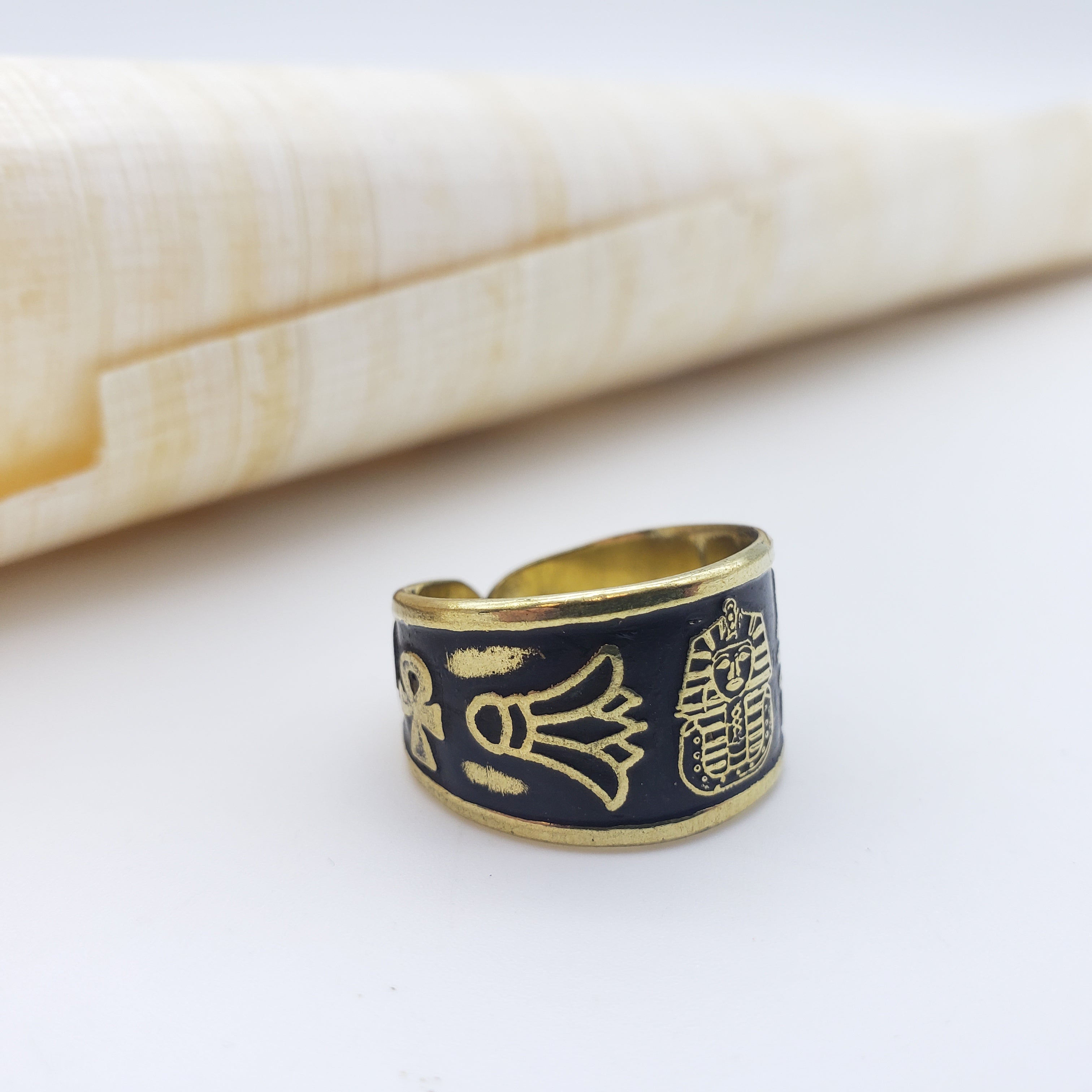 Gold and black ring with hieroglyphic designs on a white surface