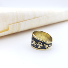 Gold and black ring with an ankh symbol on a white surface